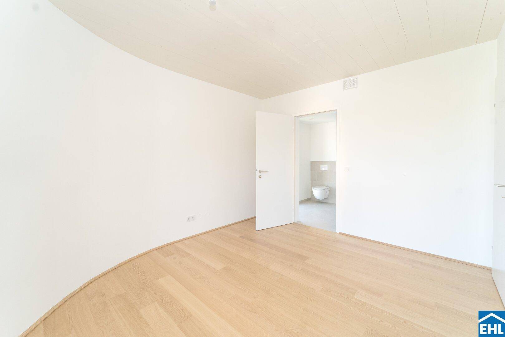 Leeres Schlafzimmer mit Parkettboden und Zugang zu einem angrenzenden Badezimmer oder WC.