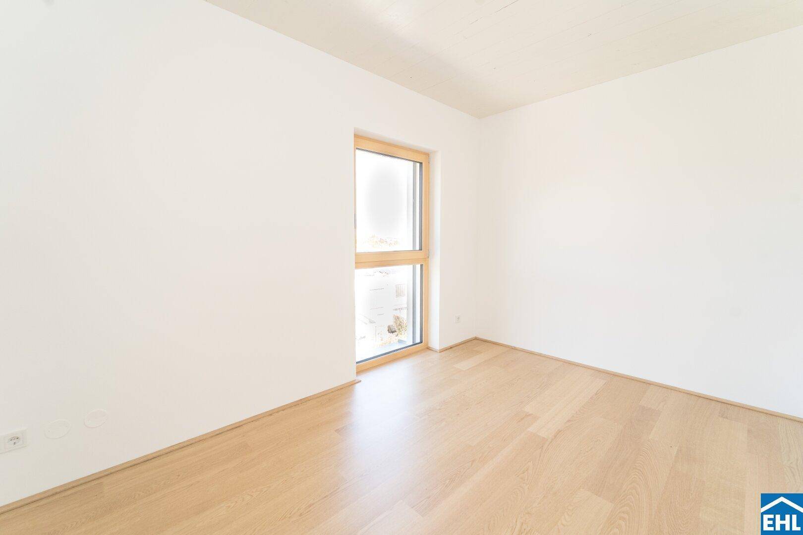 Ruhiges Schlafzimmer mit hellem Parkettboden und einem hohen Fenster für viel Tageslicht.