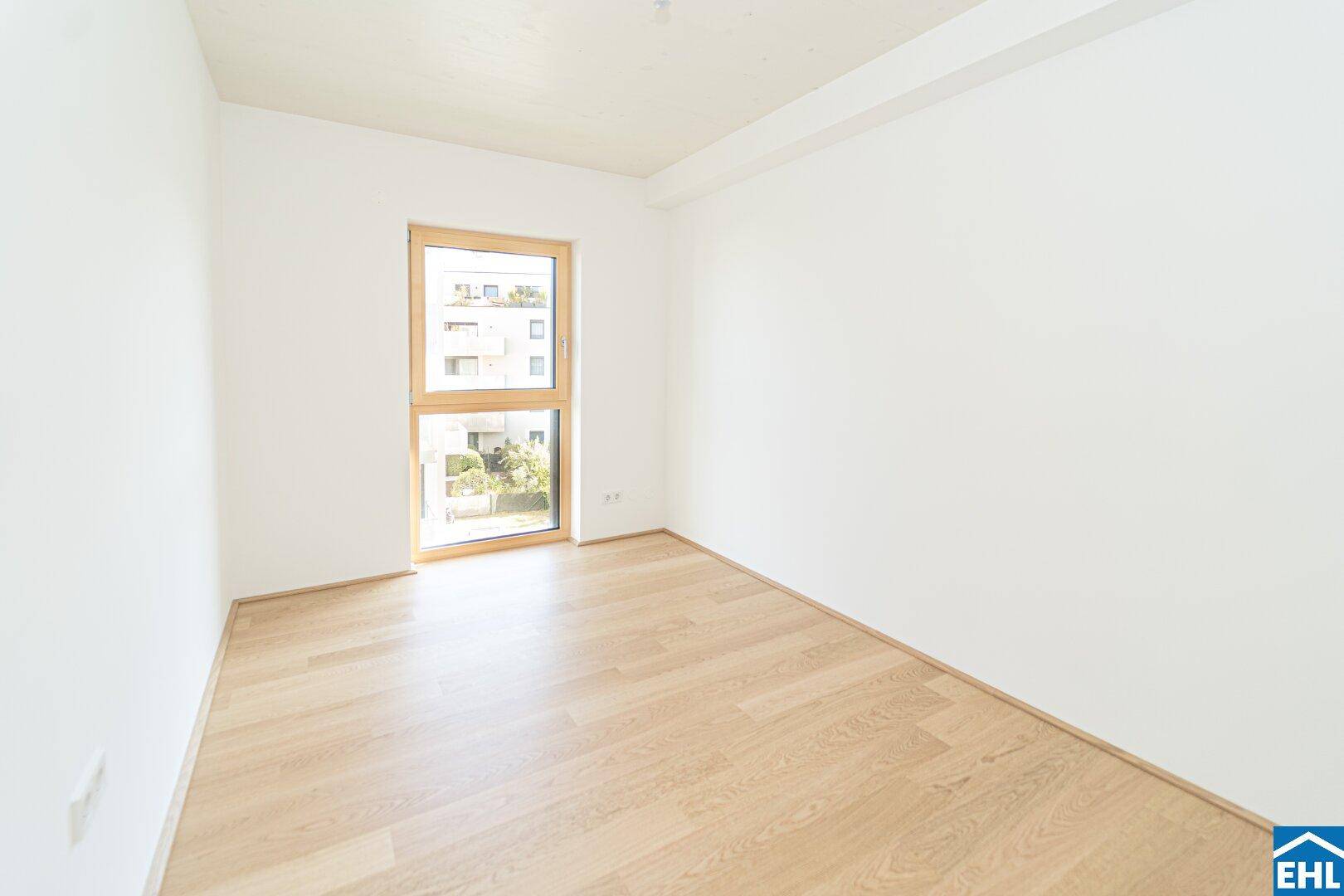 Helles Schlafzimmer mit Parkettboden und einem großen Fenster, das den Raum erhellt.