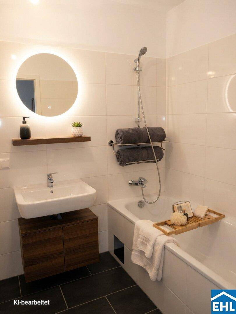 Modernes Badezimmer mit Badewanne, beleuchtetem Spiegel und dunklen Bodenfliesen.