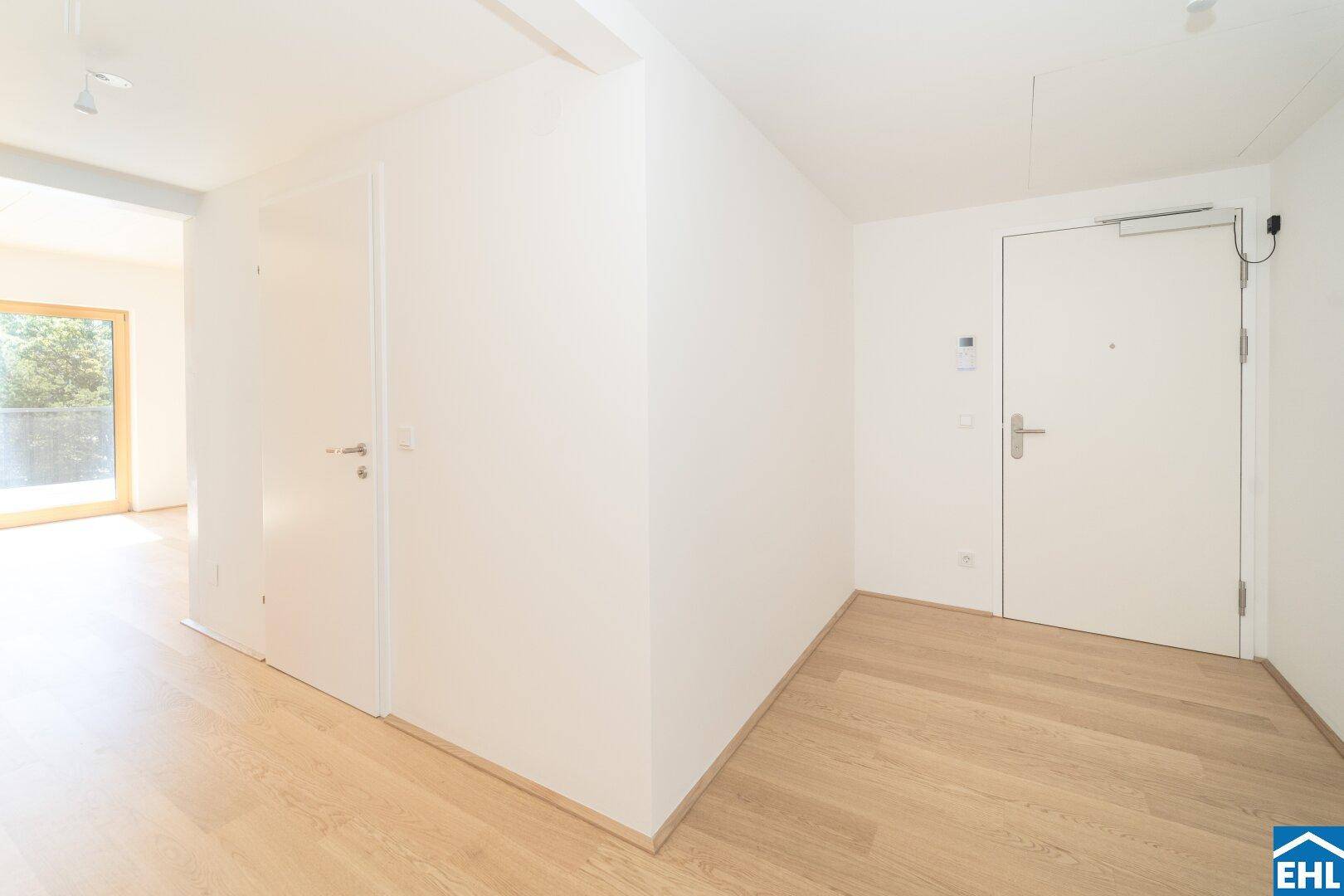 Heller Eingangsbereich mit modernem Holzparkett und weißen Wänden, der zu weiteren Räumen führt.