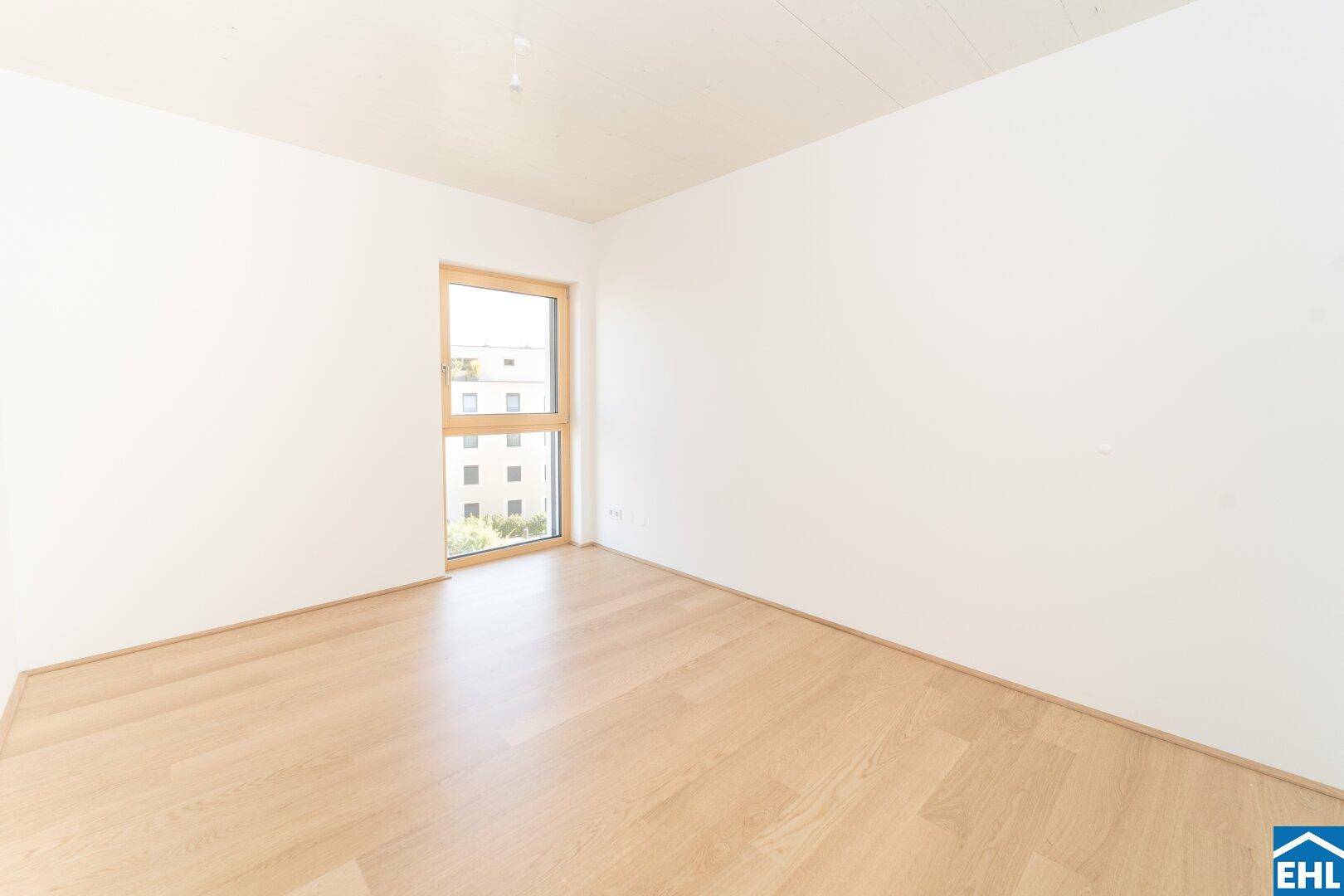 Schlafzimmer mit hellem Holzparkett und einem großen Fenster, das einen Blick nach draußen bietet.