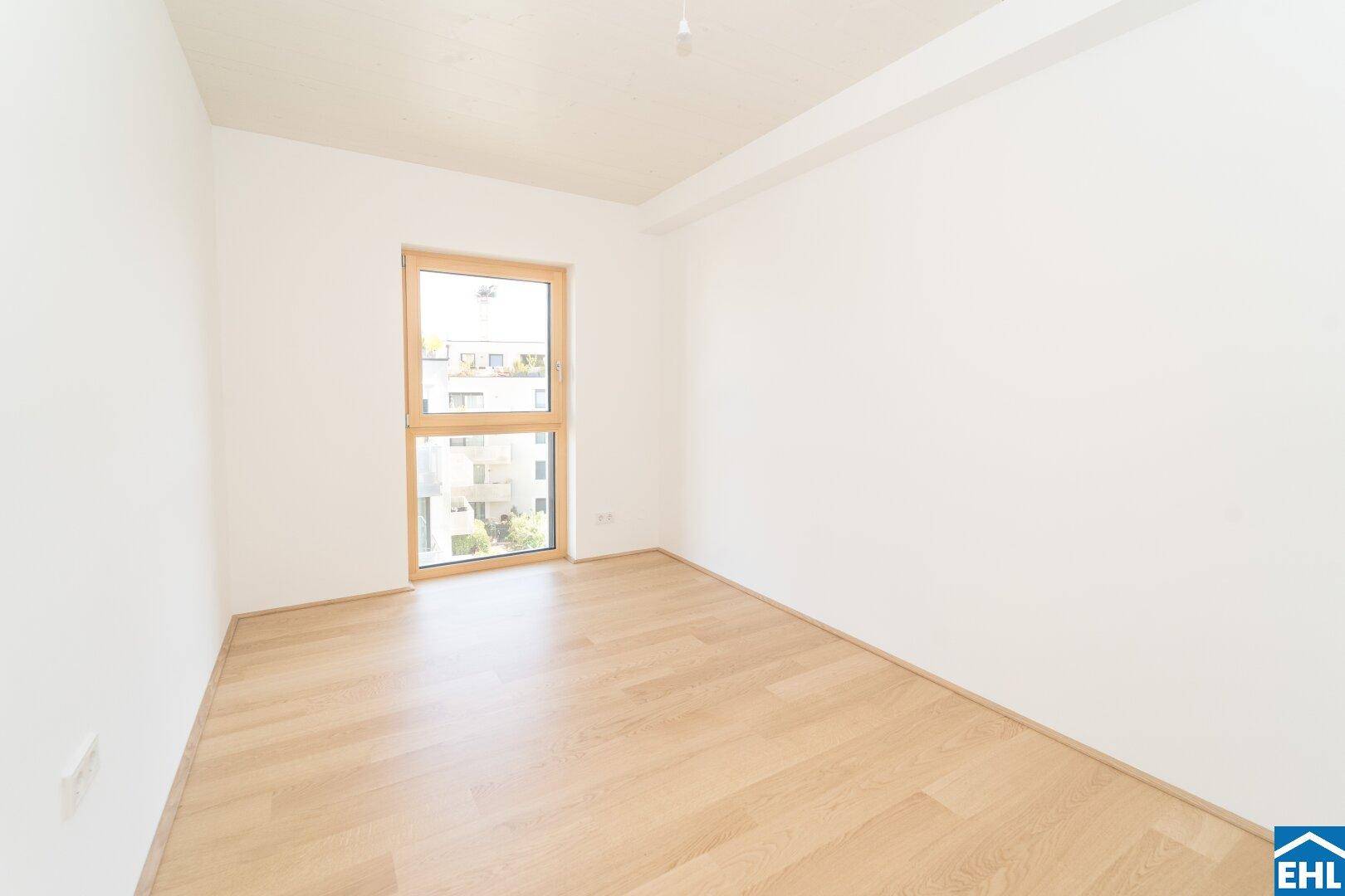 Geräumiges Zimmer mit hellem Holzparkett und einem Fenster, das viel Tageslicht in den Raum bringt.