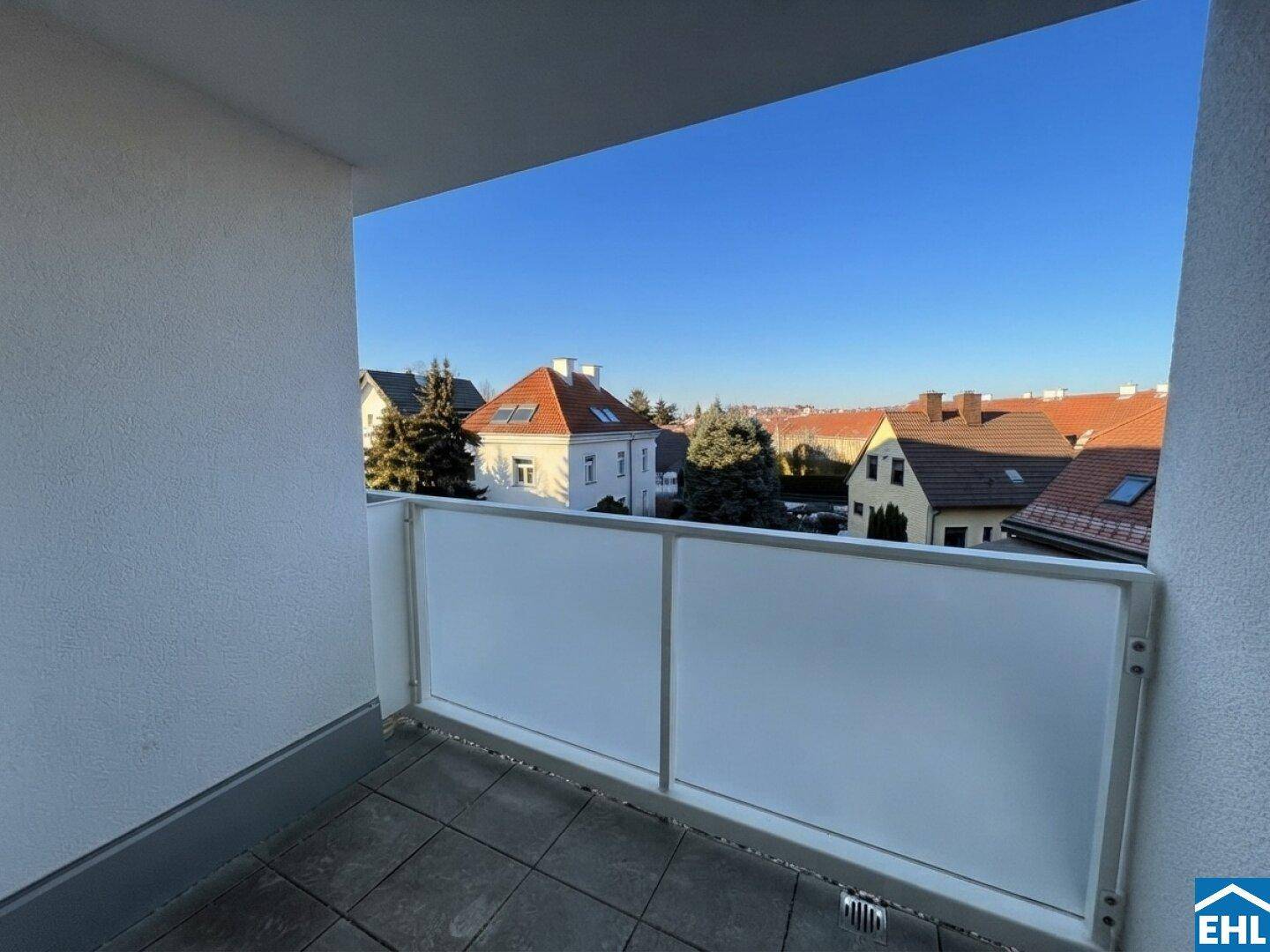 Heller Balkon mit Blick auf die umliegenden Wohnhäuser und klarem blauen Himmel.