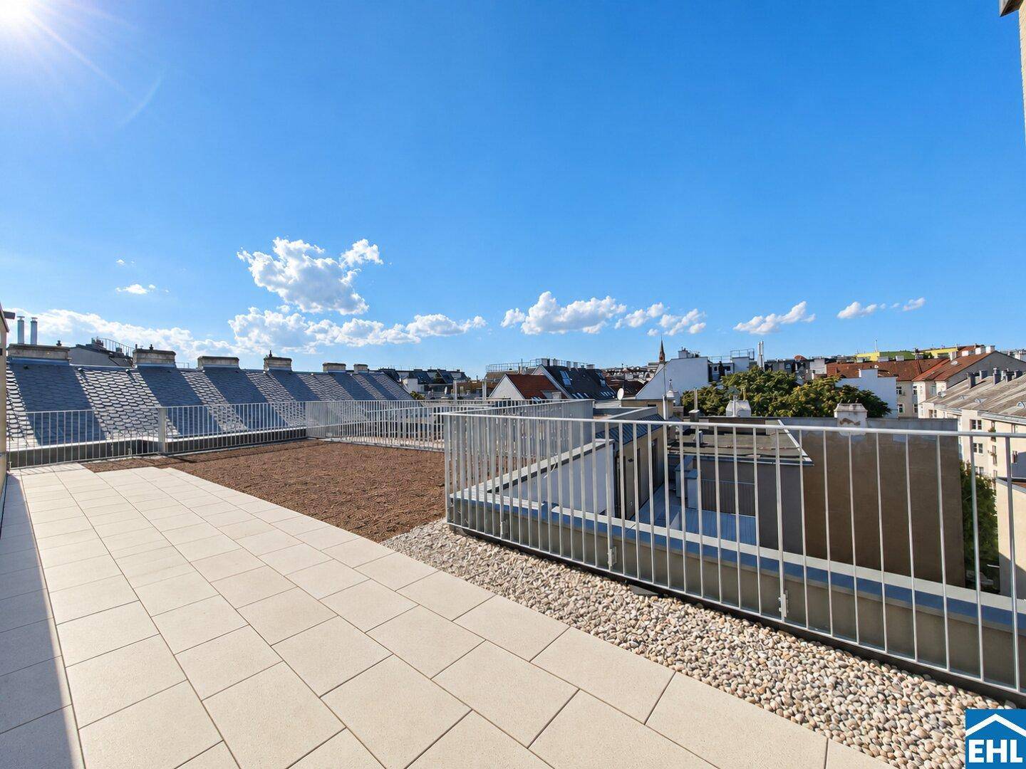 Sonniger Dachterrassenbereich mit Fliesen und Kies, umgeben von städtischen Dächern.