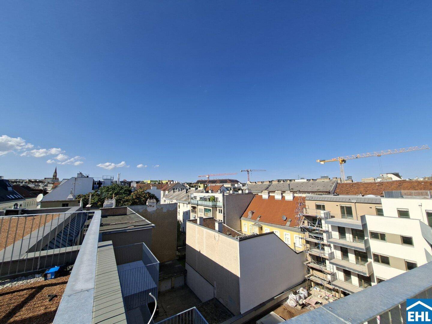 Weitläufiger Blick über die Dächer der Stadt mit Baukränen am Horizont.