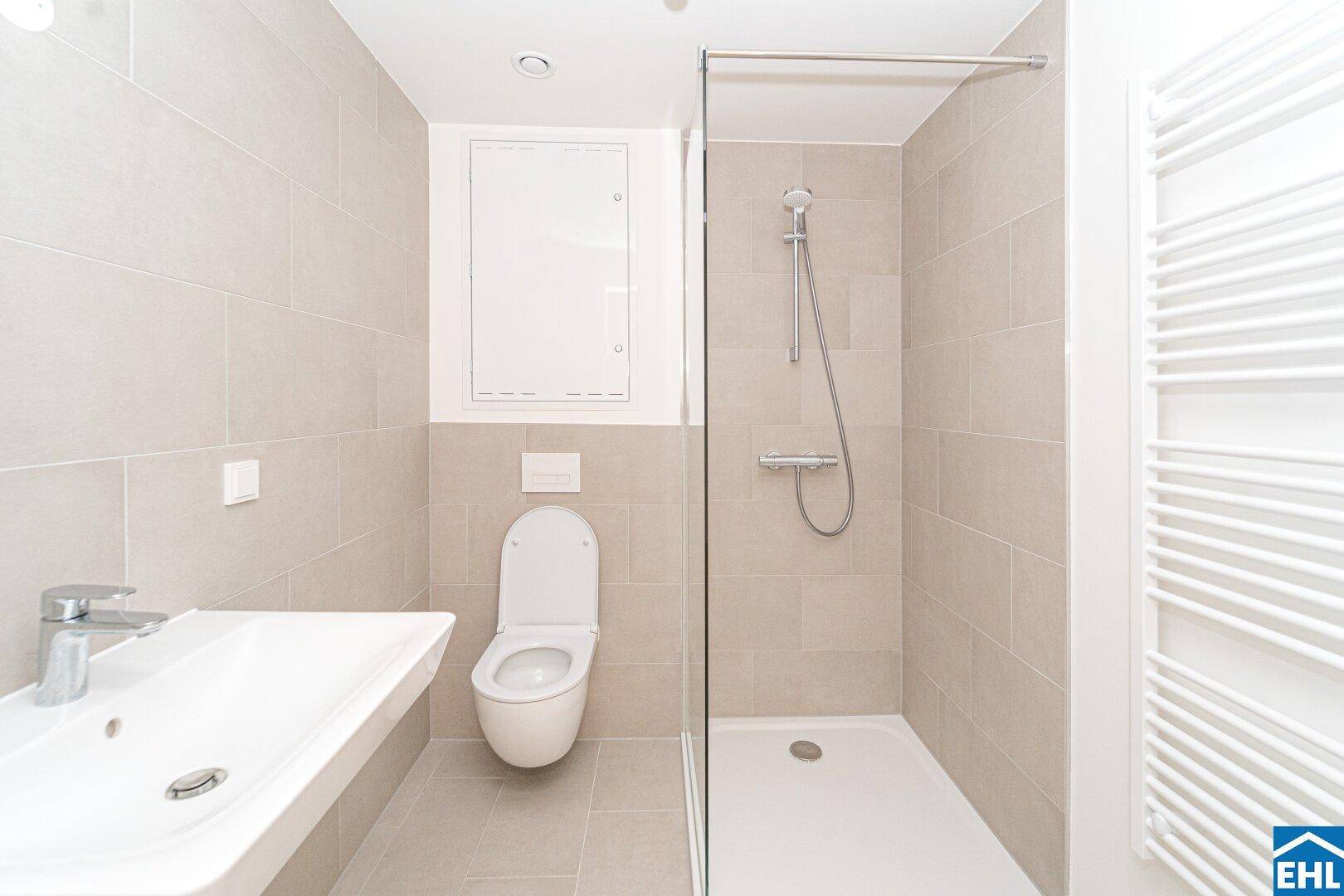 Modernes Badezimmer mit beigefarbenen Fliesen, wandhängendem WC und einer geräumigen begehbaren Dusche.