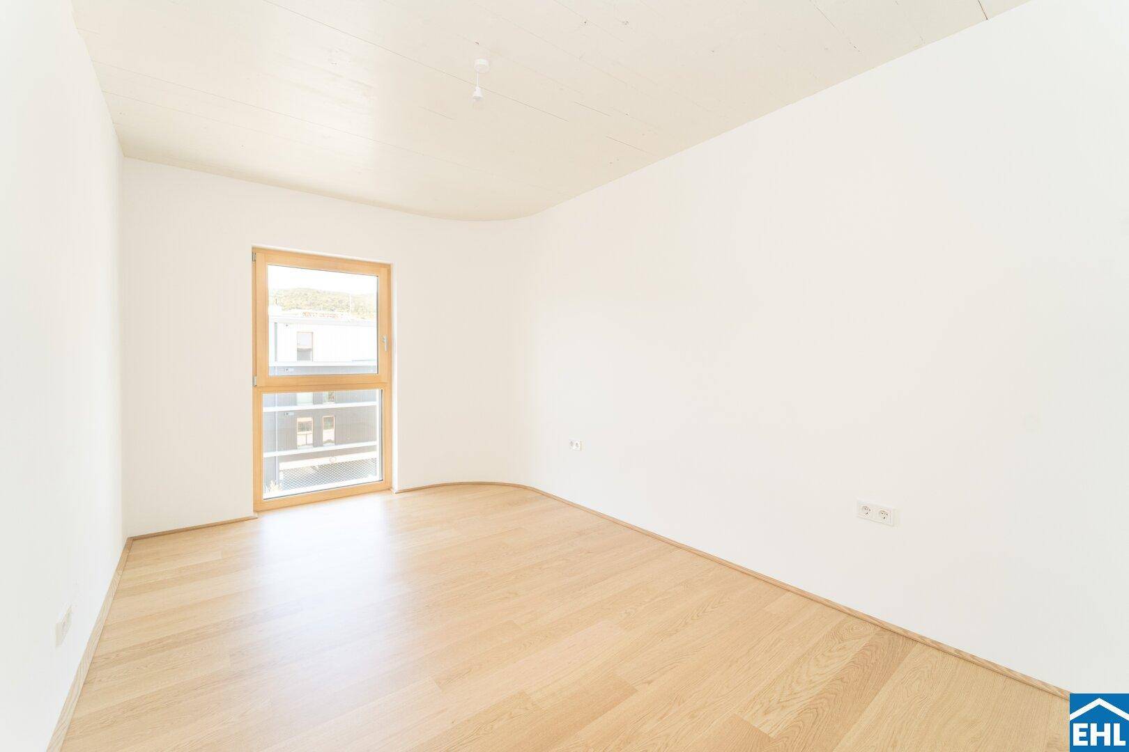 Helles Schlafzimmer mit Parkettboden, einer eleganten Rundwand und einem hohen Fenster.