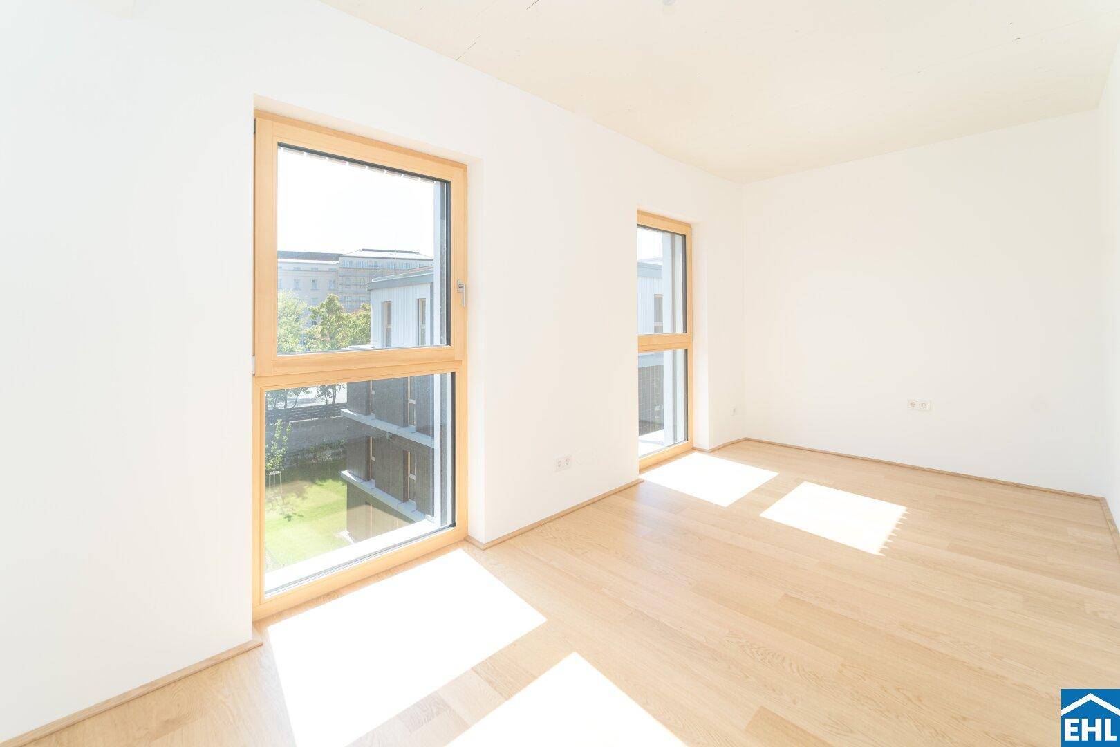 Großzügiges Schlafzimmer mit viel Tageslicht, hellem Parkettboden und zwei großen Fenstern.