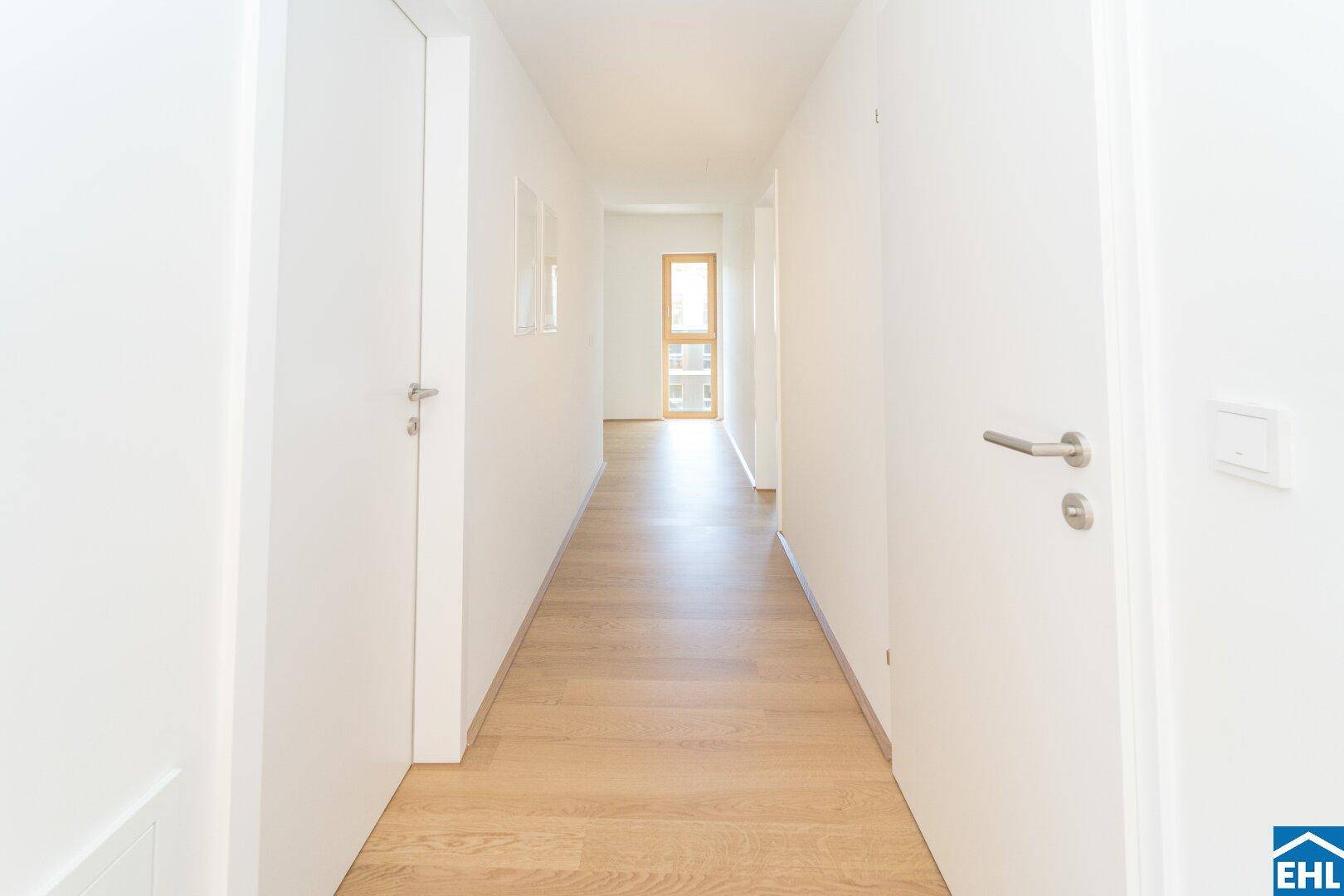 Langer, heller Flur mit Parkettboden und natürlichem Lichteinfall durch ein Fenster am Ende.