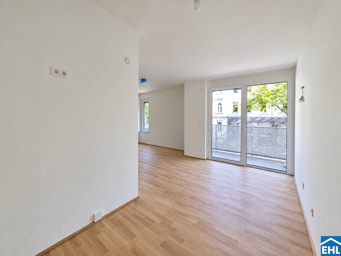Heller Wohnbereich mit Parkettboden und Zugang zu einem Balkon mit Blick ins Grüne.