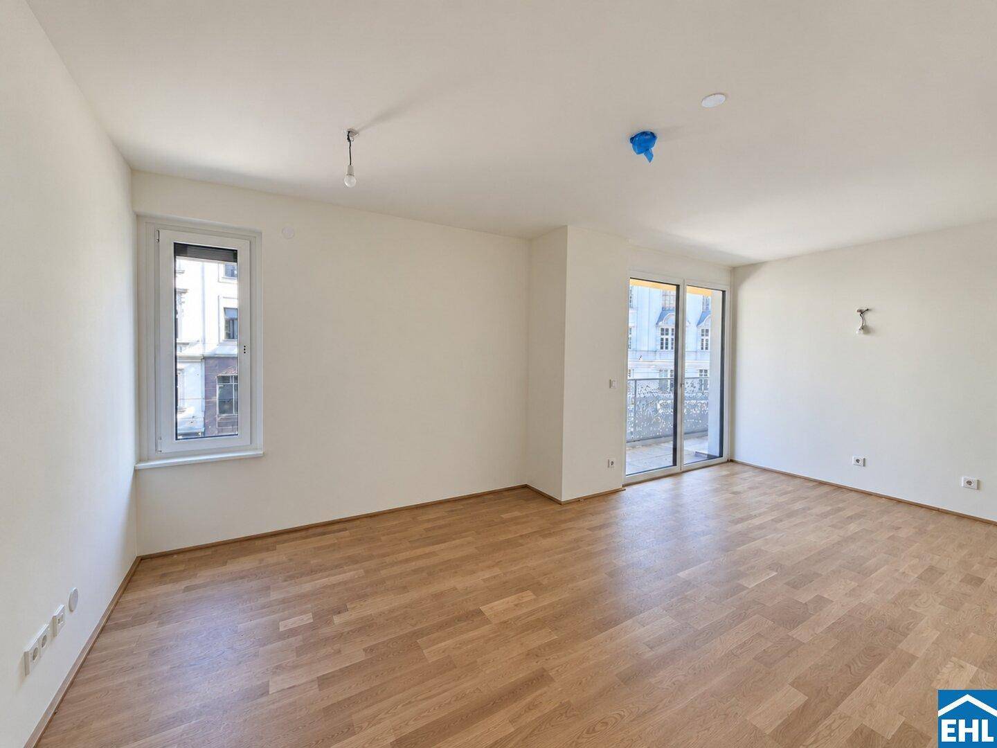 Lichtdurchfluteter Raum mit Parkettboden, großem Fenster und Zugang zum Außenbereich.