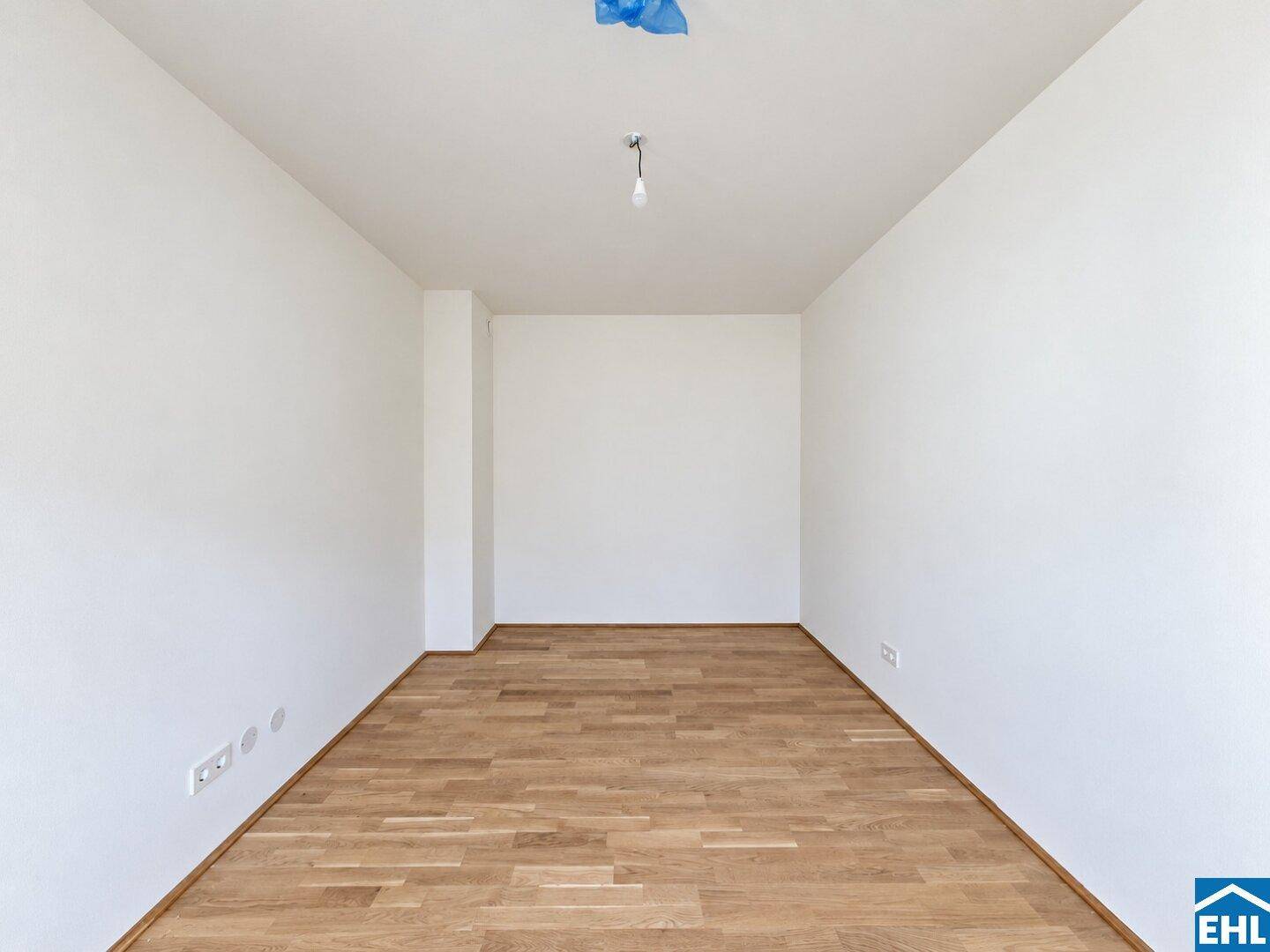 Leerer Raum mit weißen Wänden und hellem Parkettboden, bereit zur individuellen Gestaltung in einem Neubau.