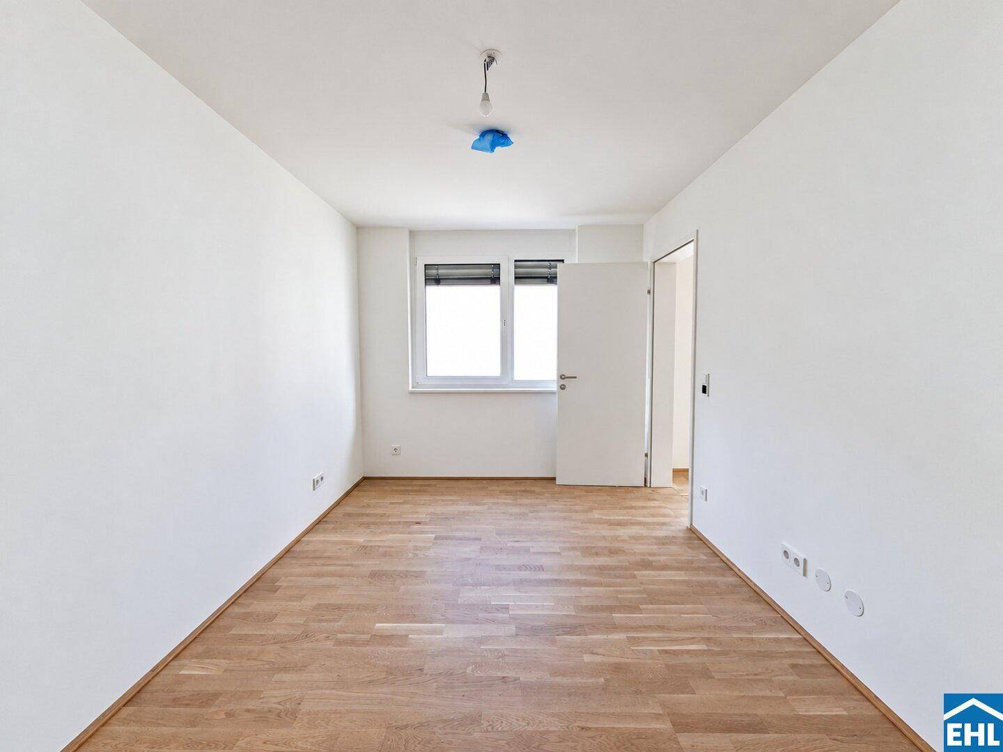 Helles Schlafzimmer mit Parkettboden und einem Fenster mit Rollladen, ideal für Ruhe und Erholung.