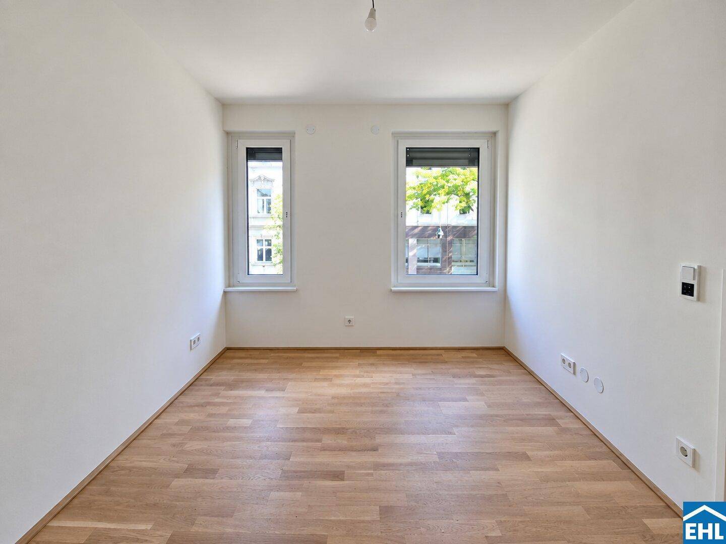Leeres Zimmer mit Parkettboden und zwei Fenstern, ideal als Schlaf- oder Arbeitszimmer.