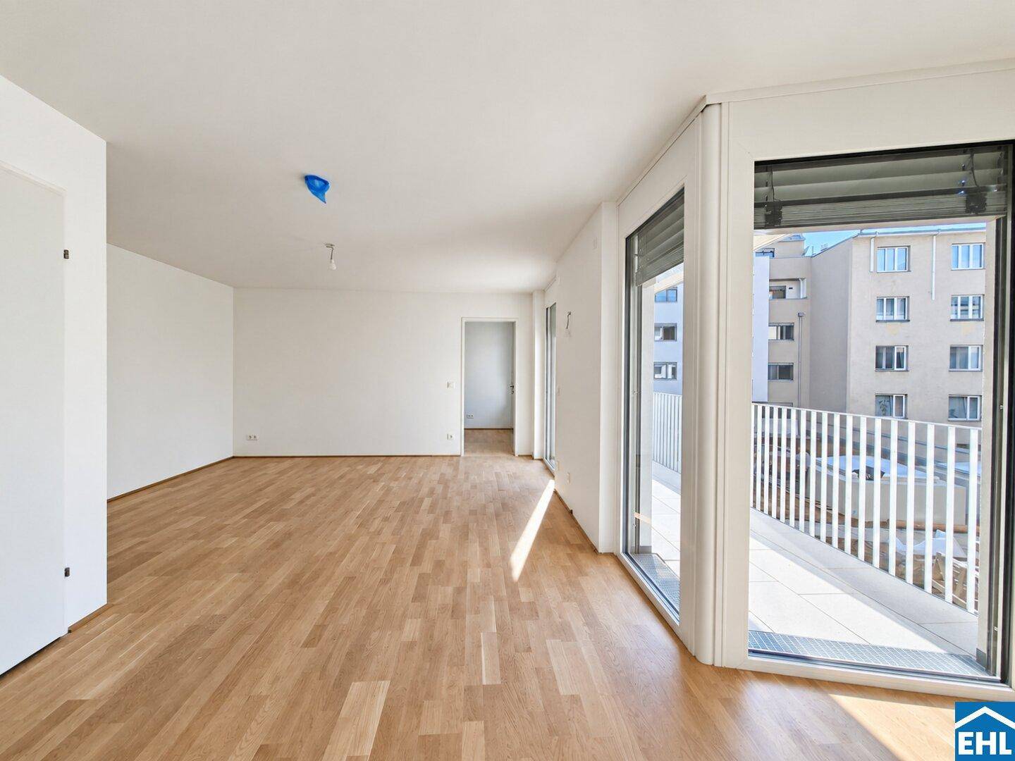 Geräumiges, helles Wohnzimmer mit Holzboden und Blick auf die umliegenden Gebäude von einem Balkon.