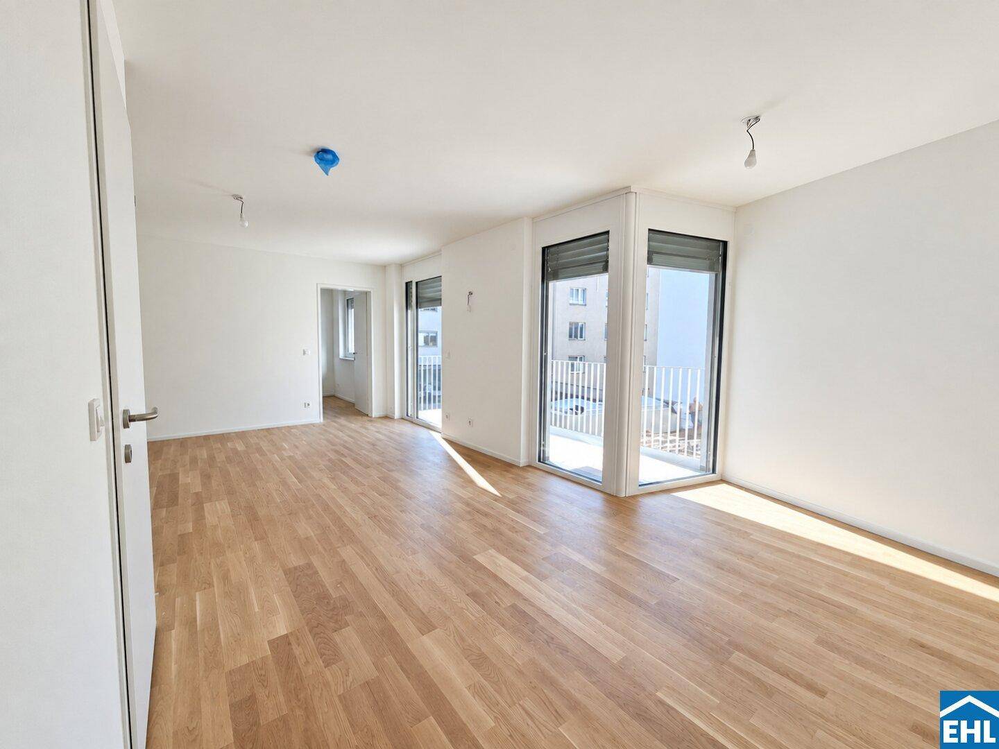 Lichtdurchfluteter Wohnbereich mit Parkettboden und mehreren Fenstertüren zum Außenbereich mit Rollläden.