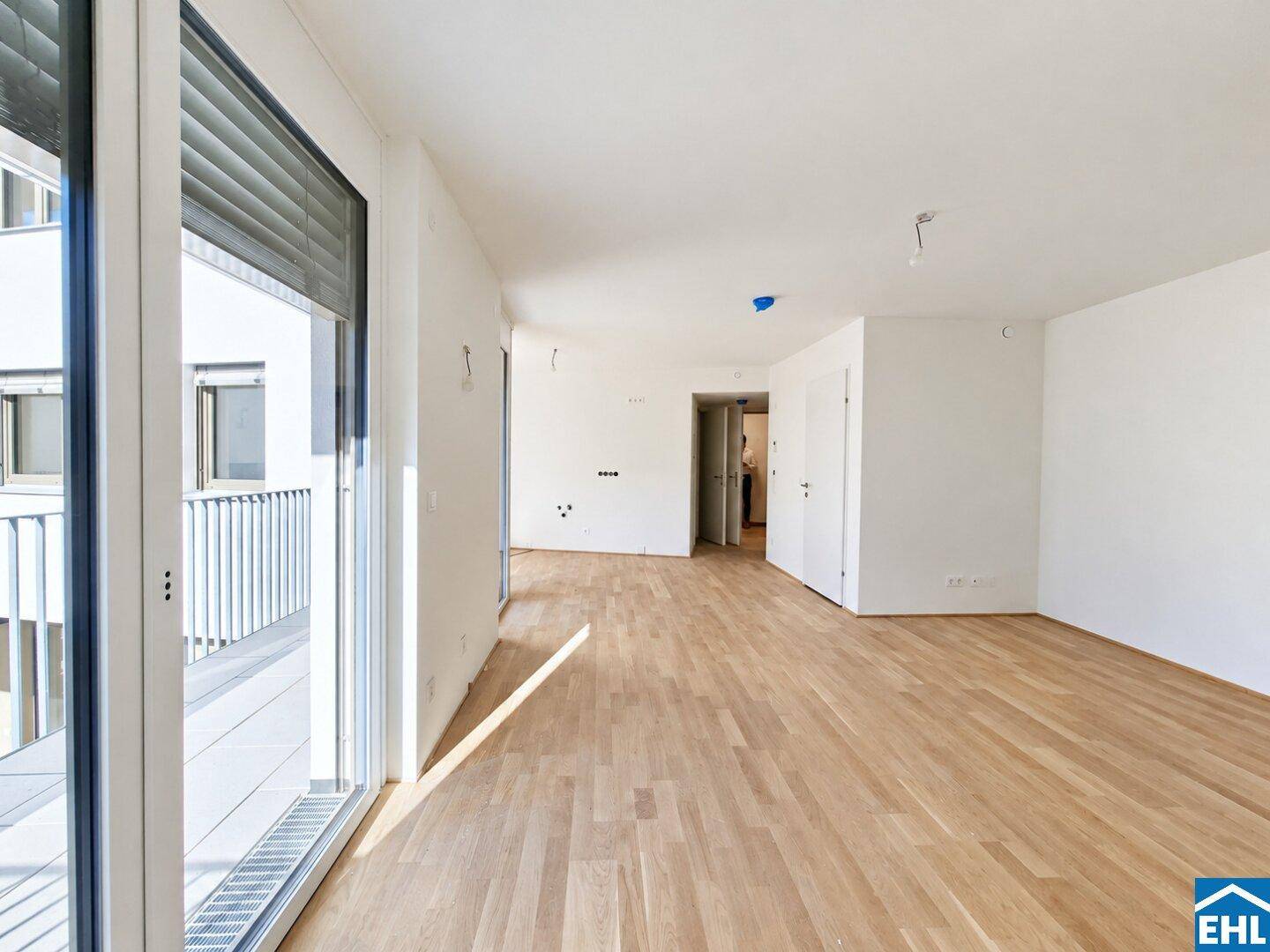 Heller Wohnraum mit Parkett und breiten Fenstern, die viel Tageslicht hereinlassen und einen Balkon bieten.