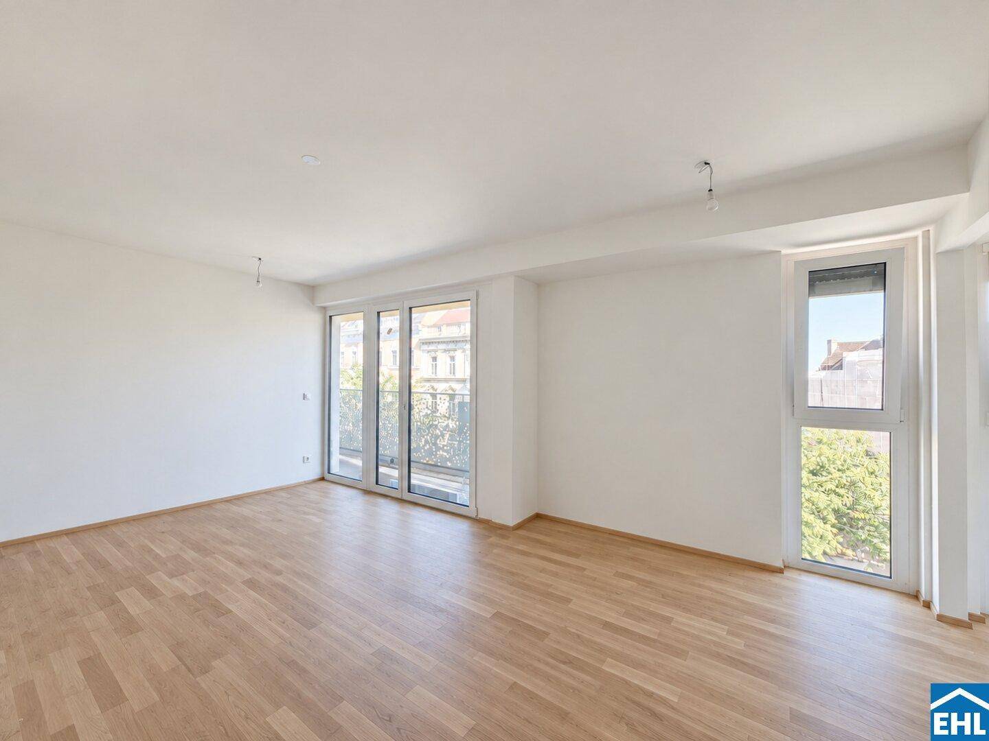 Heller Wohnraum mit Holzboden und großen Fenstern, die viel Tageslicht hereinlassen.