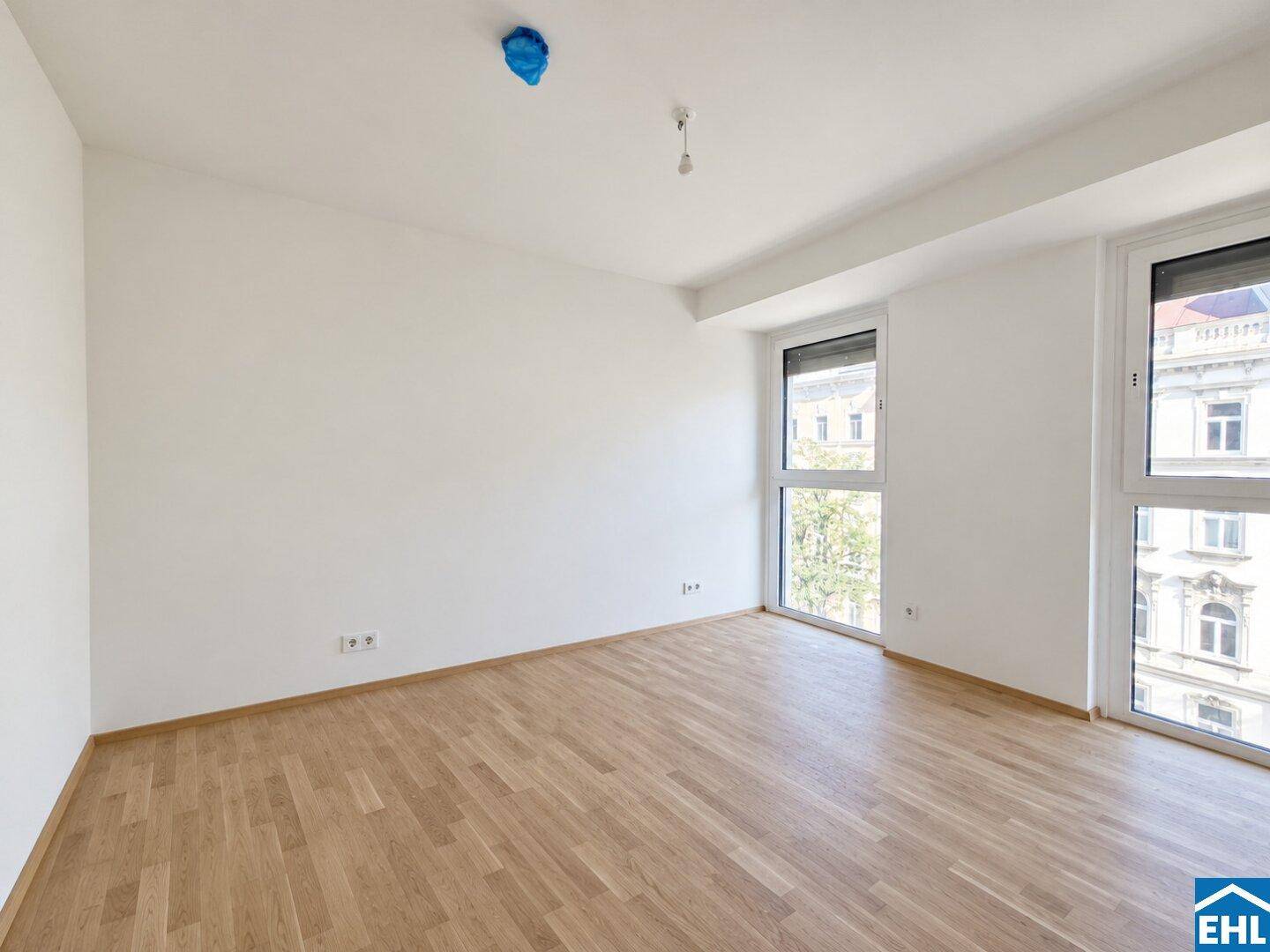 Geräumiger, heller Raum mit Holzboden und zwei Fenstern, die einen Blick nach draußen bieten.