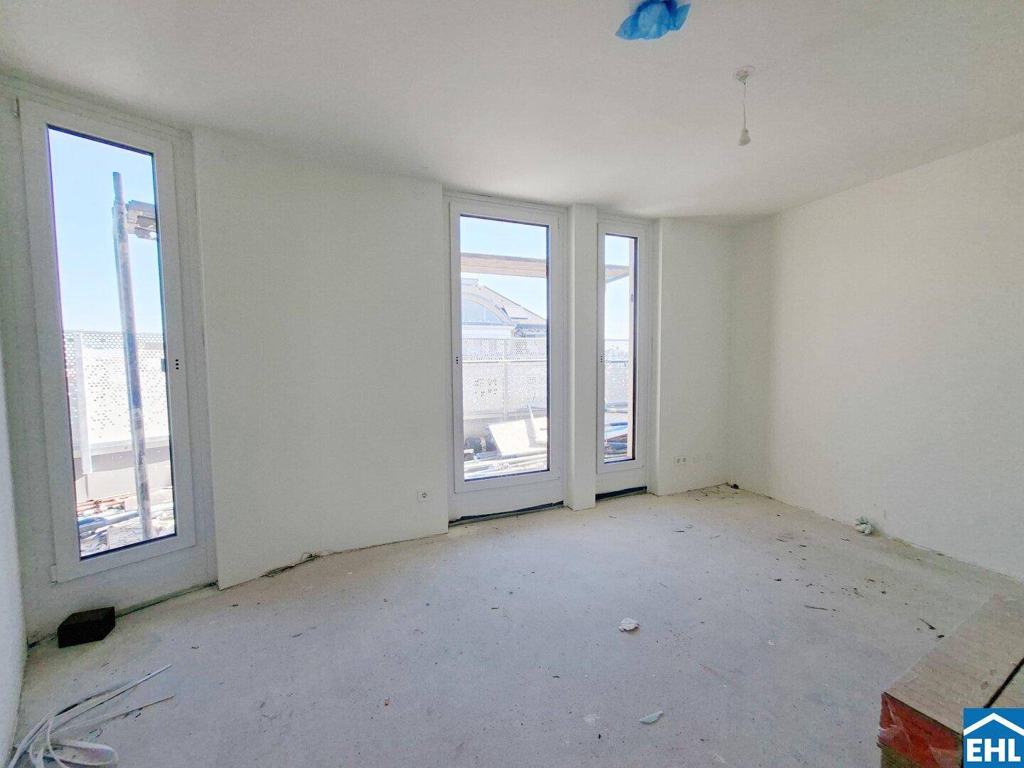 Geräumiger, unfertiger Wohnraum mit großen Fenstern und Zugang zu einem im Bau befindlichen Außenbereich.