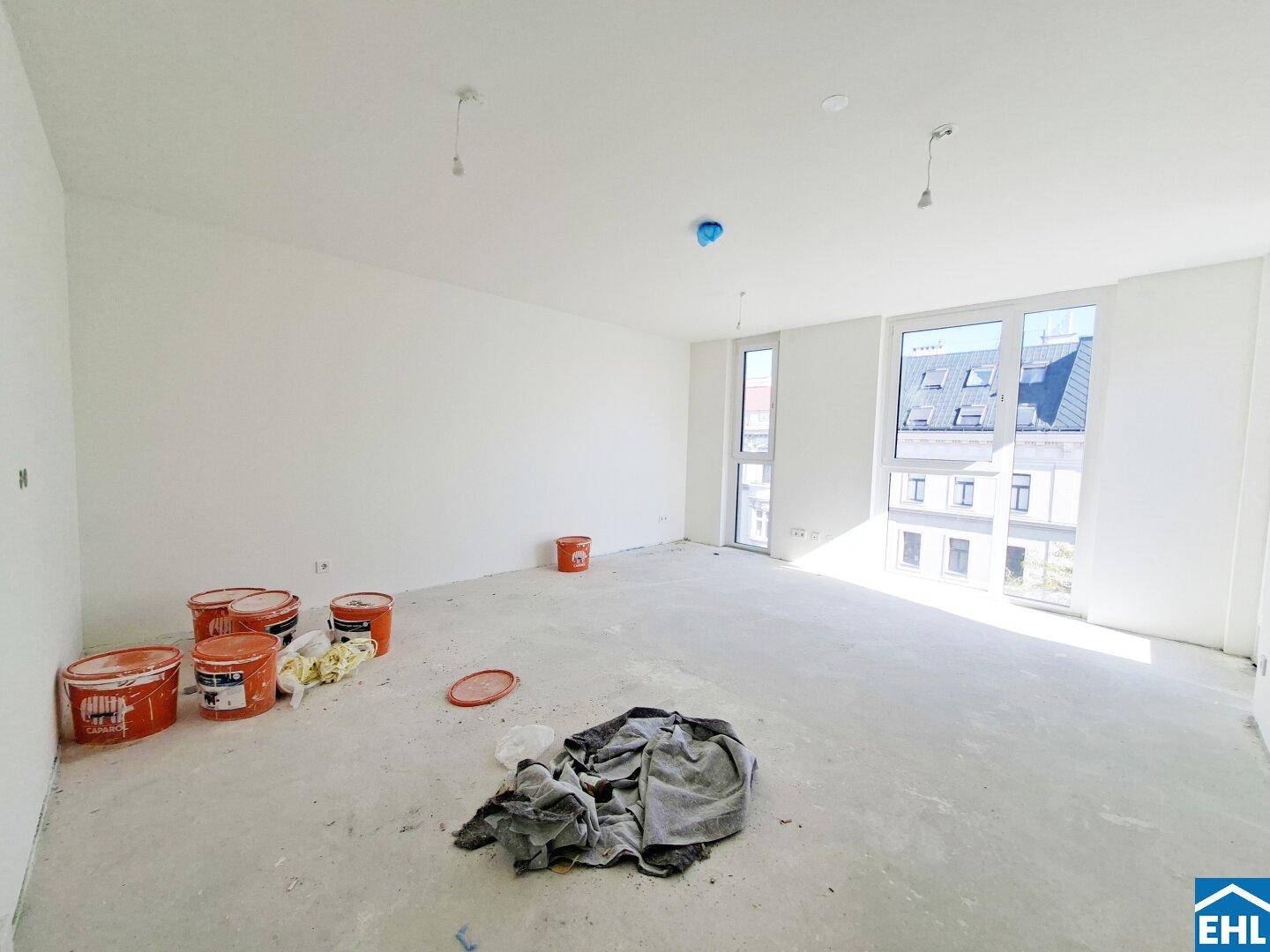 Großer, heller Wohnraum im Rohbau mit mehreren Fenstern und Blick auf die umliegenden Gebäude.