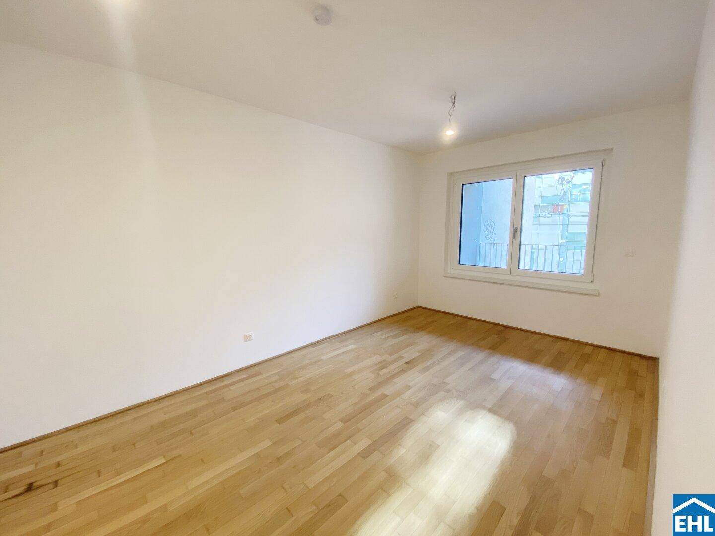 Helles Schlafzimmer mit Parkettboden, weißen Wänden und großem Fenster.