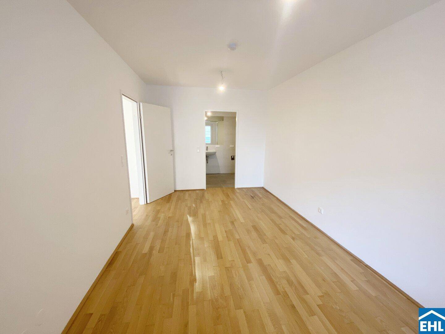 Leeres Zimmer mit hellem Parkettboden und Zugang zu einem weiteren Raum.
