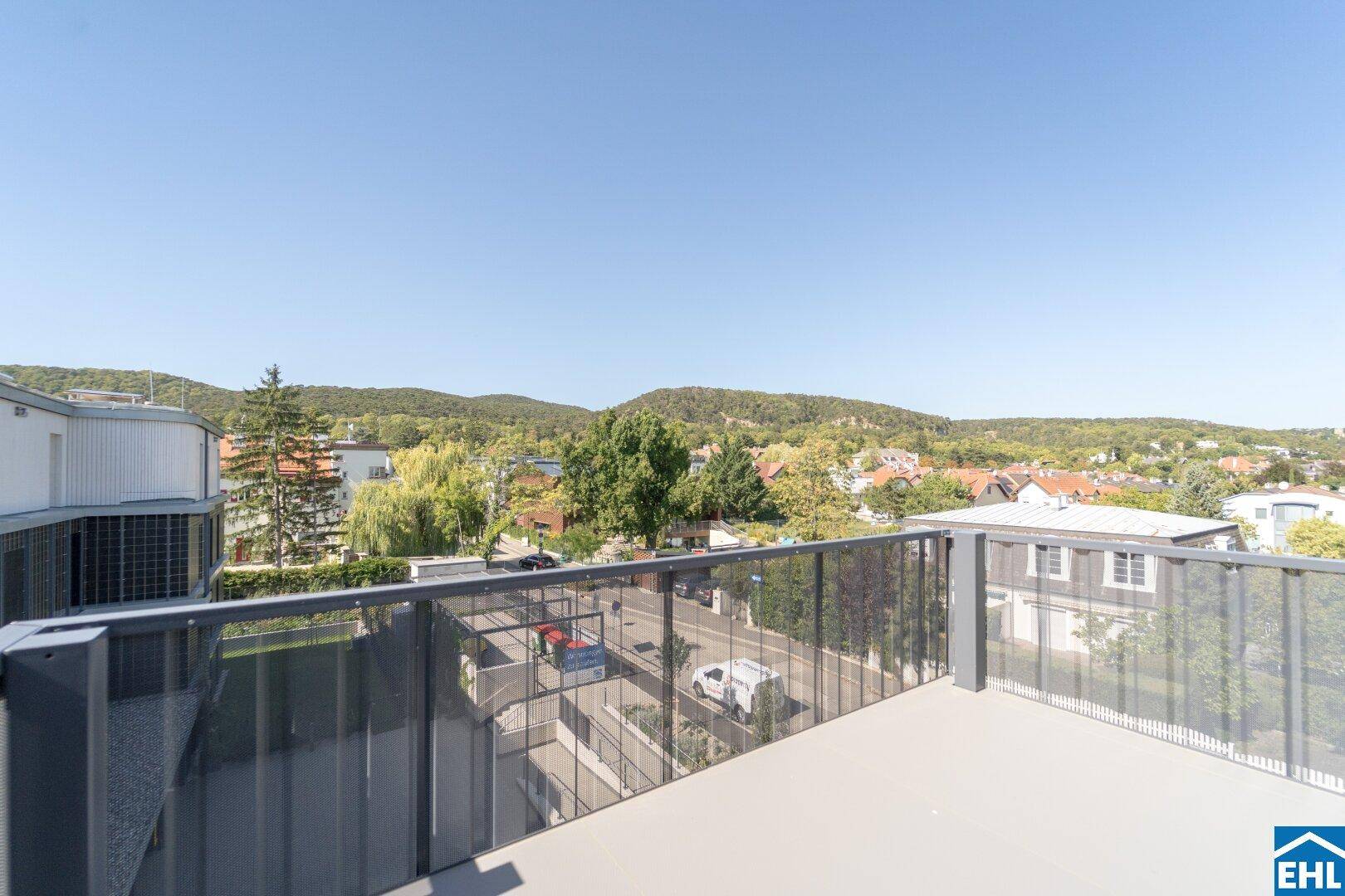 Aussicht vom Balkon mit moderner Brüstung über die Wohnanlage und die grüne Hügellandschaft.