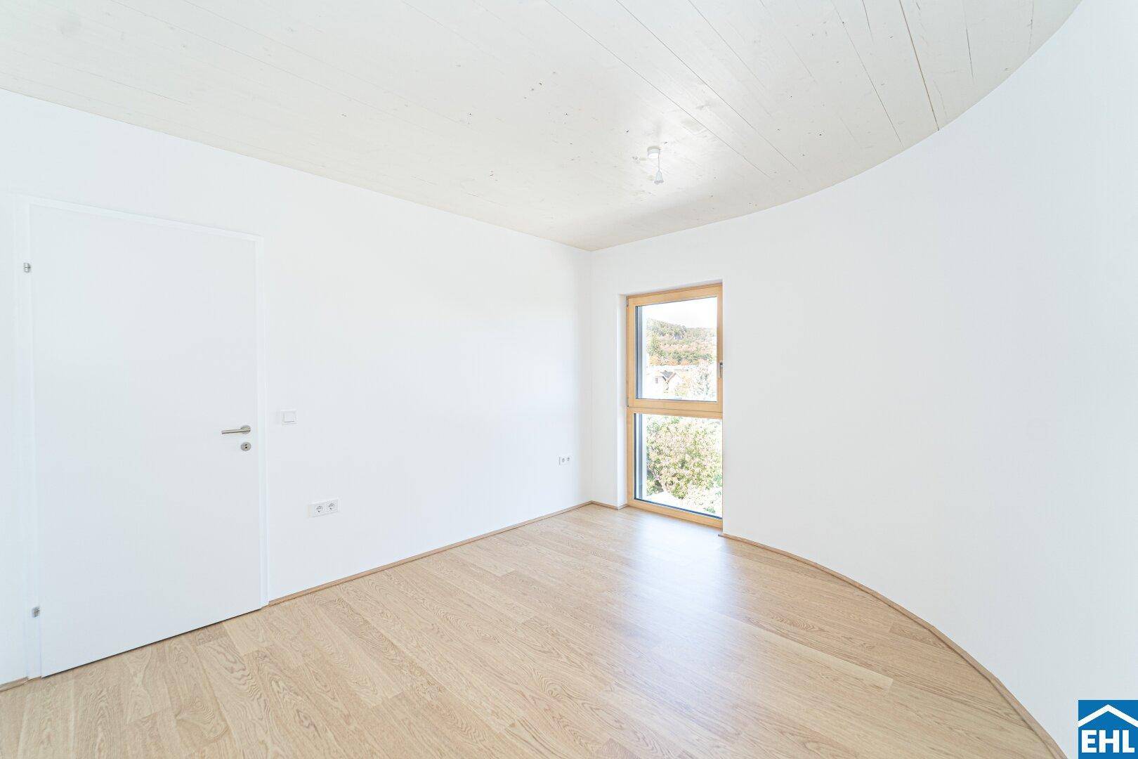 Helles Schlafzimmer mit Holzboden und einem Fenster, das einen Blick ins Grüne bietet.