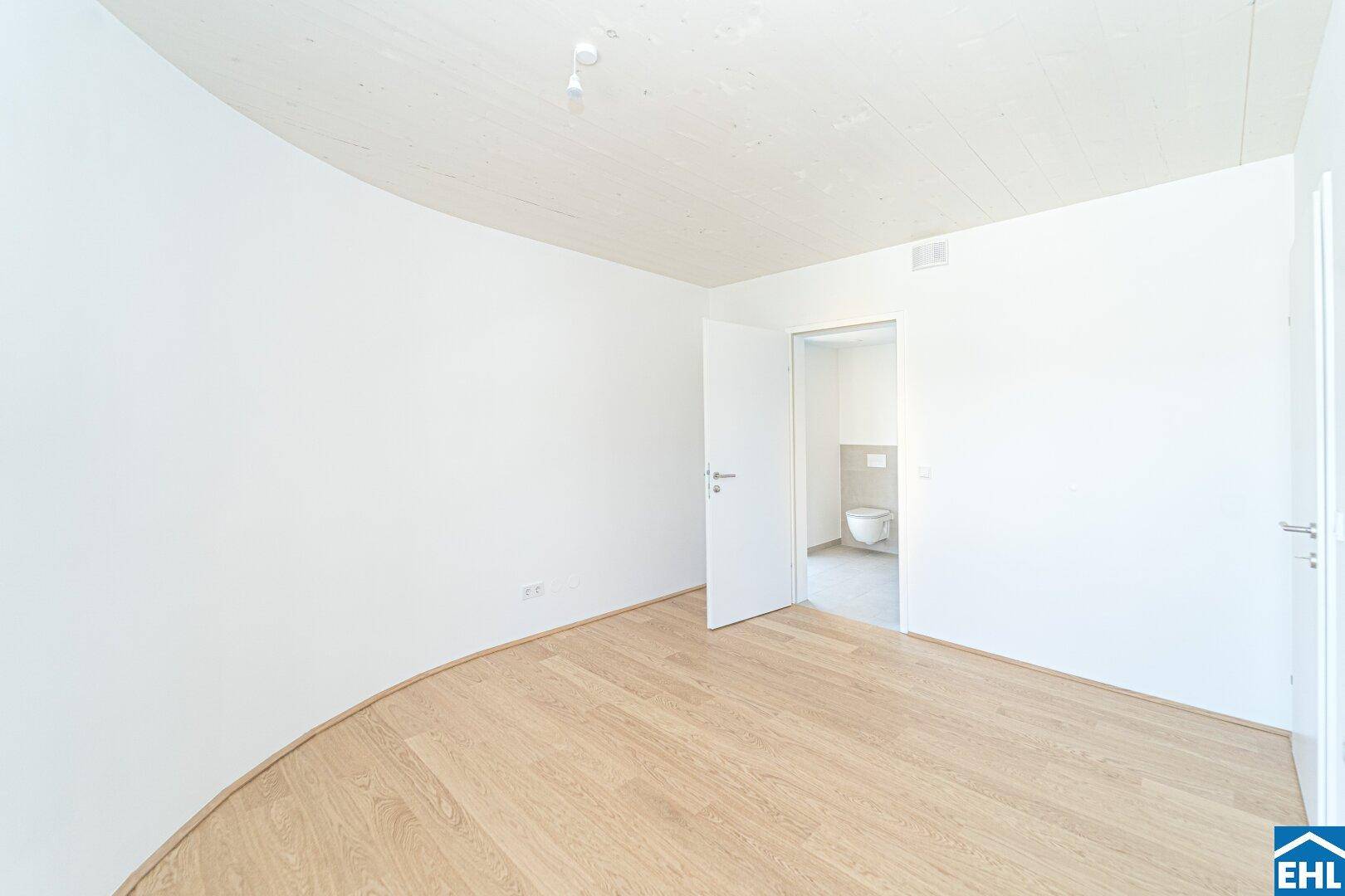 Heller Raum mit Holzboden und Zugang zu einem modernen Badezimmer mit Wand-WC.