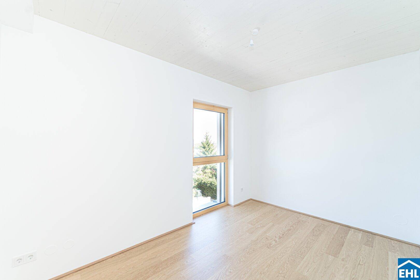 Ruhiges Schlafzimmer mit hellem Holzboden und einem Fenster, das einen Blick auf Bäume freigibt.