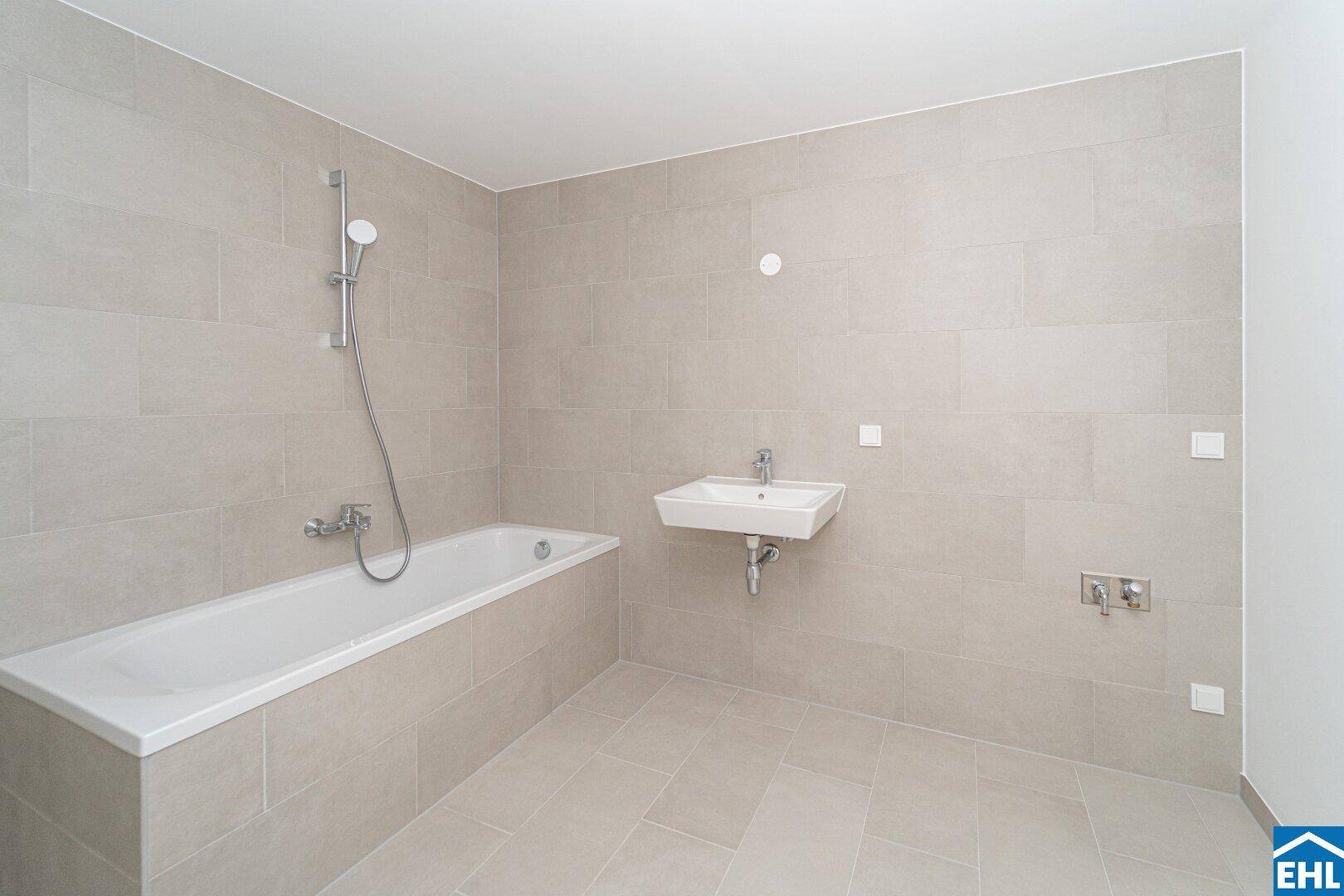 Helles Badezimmer mit Badewanne, Einzelwaschbecken und modernen hellgrauen Fliesen.