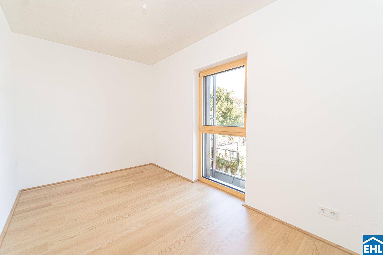 Ruhiges Schlafzimmer mit hellem Holzfußboden und einem Fenster mit Blick ins Grüne.
