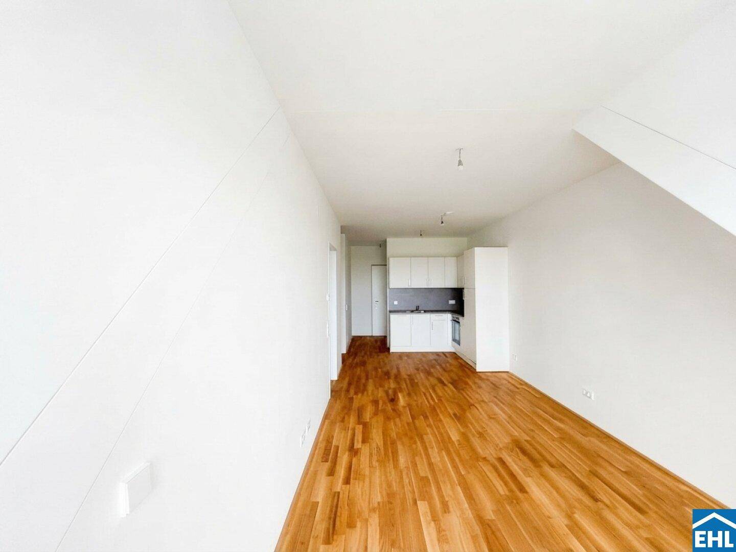 Offener Wohnbereich mit integrierter Küchenzeile und Holzboden im Dachgeschoss.