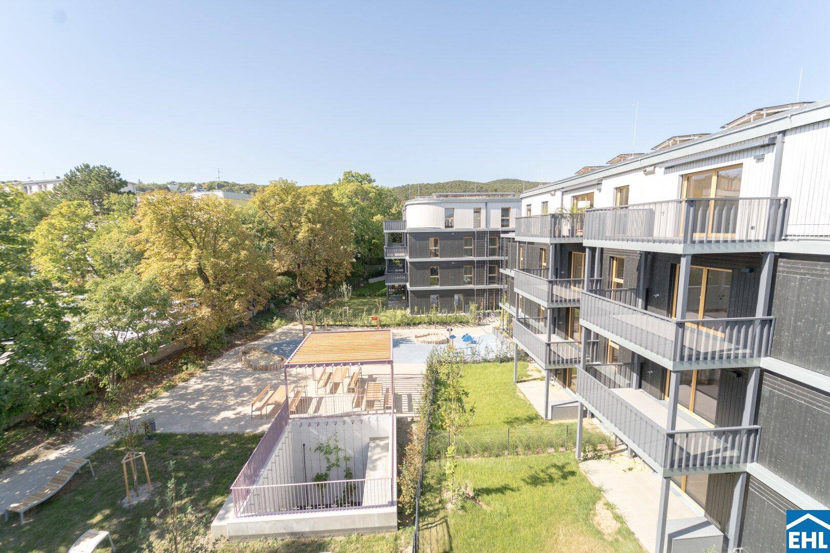 Blick von oben auf die modernen Wohngebäude mit Balkonen und den gemeinschaftlichen Gartenbereich mit Spielplatz.