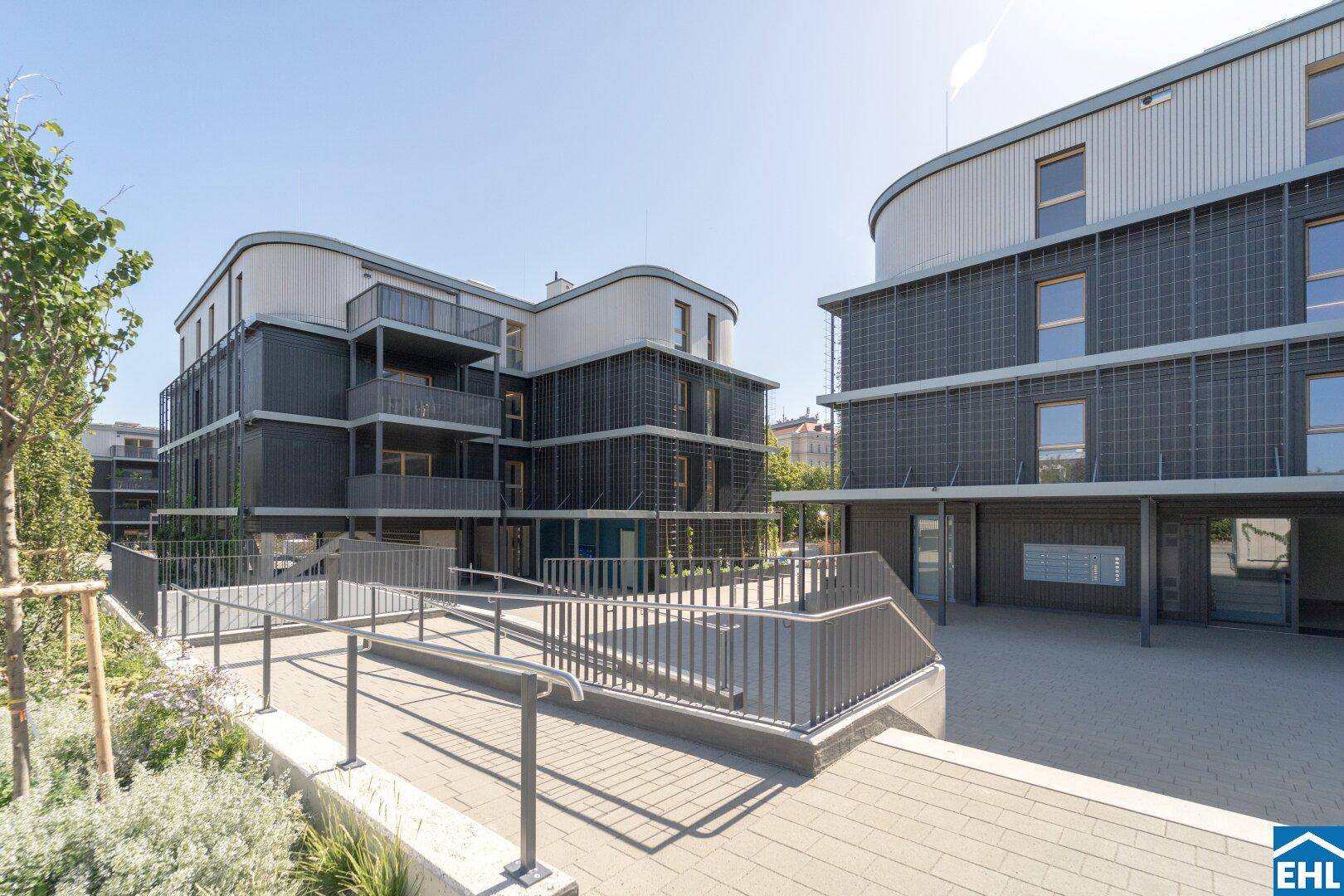 Moderne Wohngebäude mit barrierefreiem Zugang über eine Rampe und gepflasterten Wegen im Außenbereich.