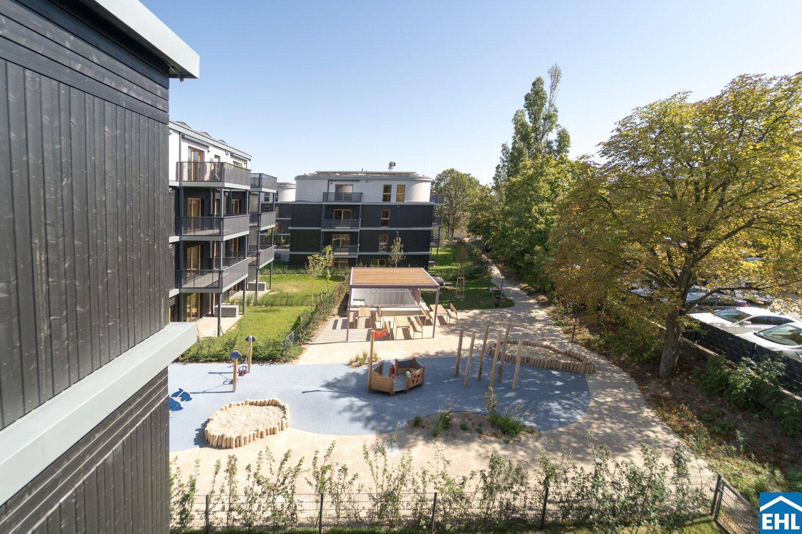 Blick von einem Balkon auf den gemeinschaftlichen Spielplatz und die umliegenden Gebäude.