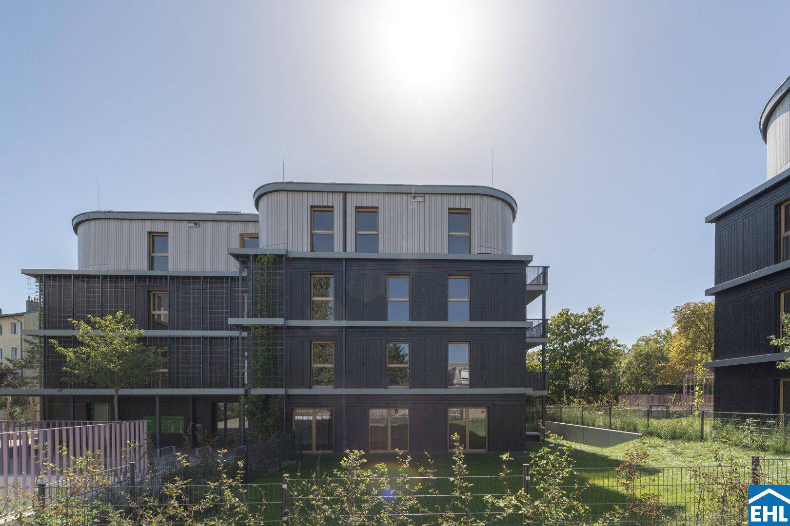 Moderne Wohngebäude mit dunkler Fassade und hellen Dachelementen unter blauem Himmel.