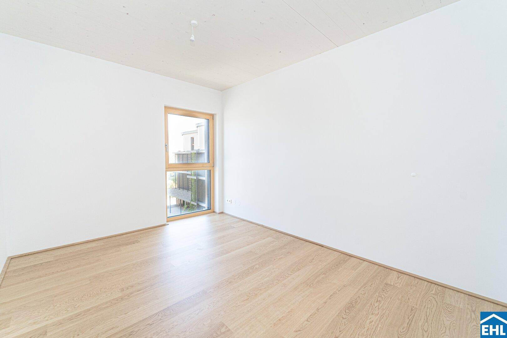 Helles Schlafzimmer mit Holzboden und einem großen Fenster mit Ausblick.