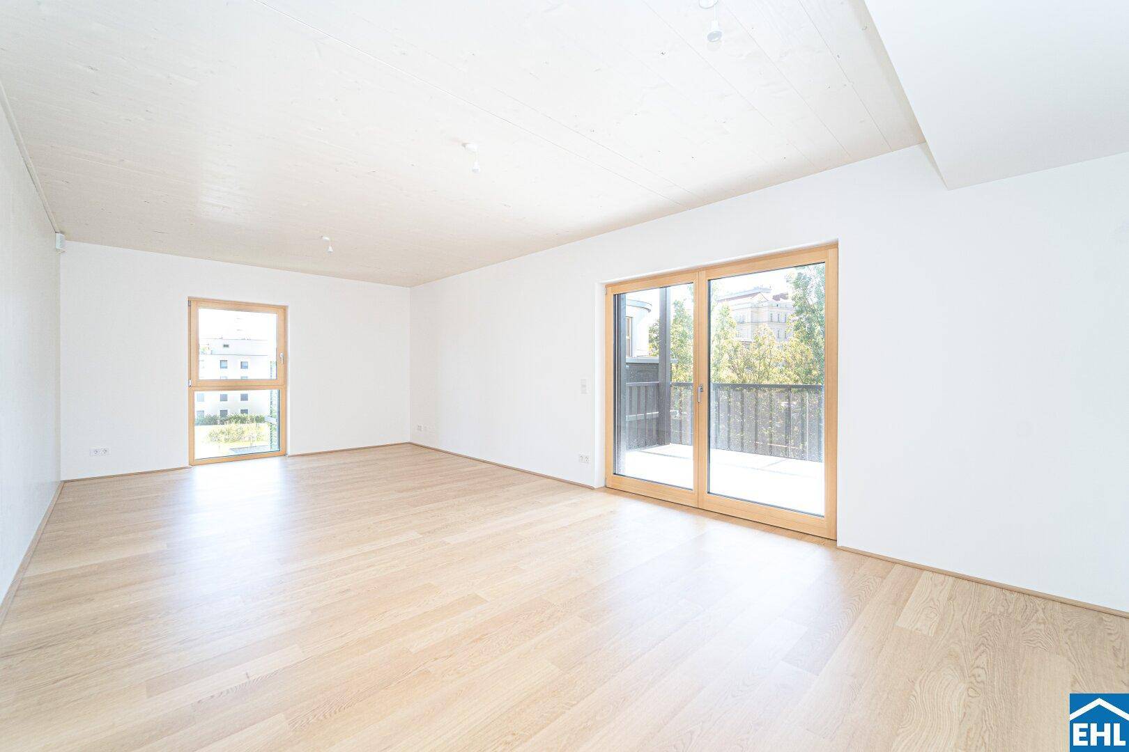 Lichtdurchflutetes Wohnzimmer mit Holzboden und zwei großen Fensterfronten.