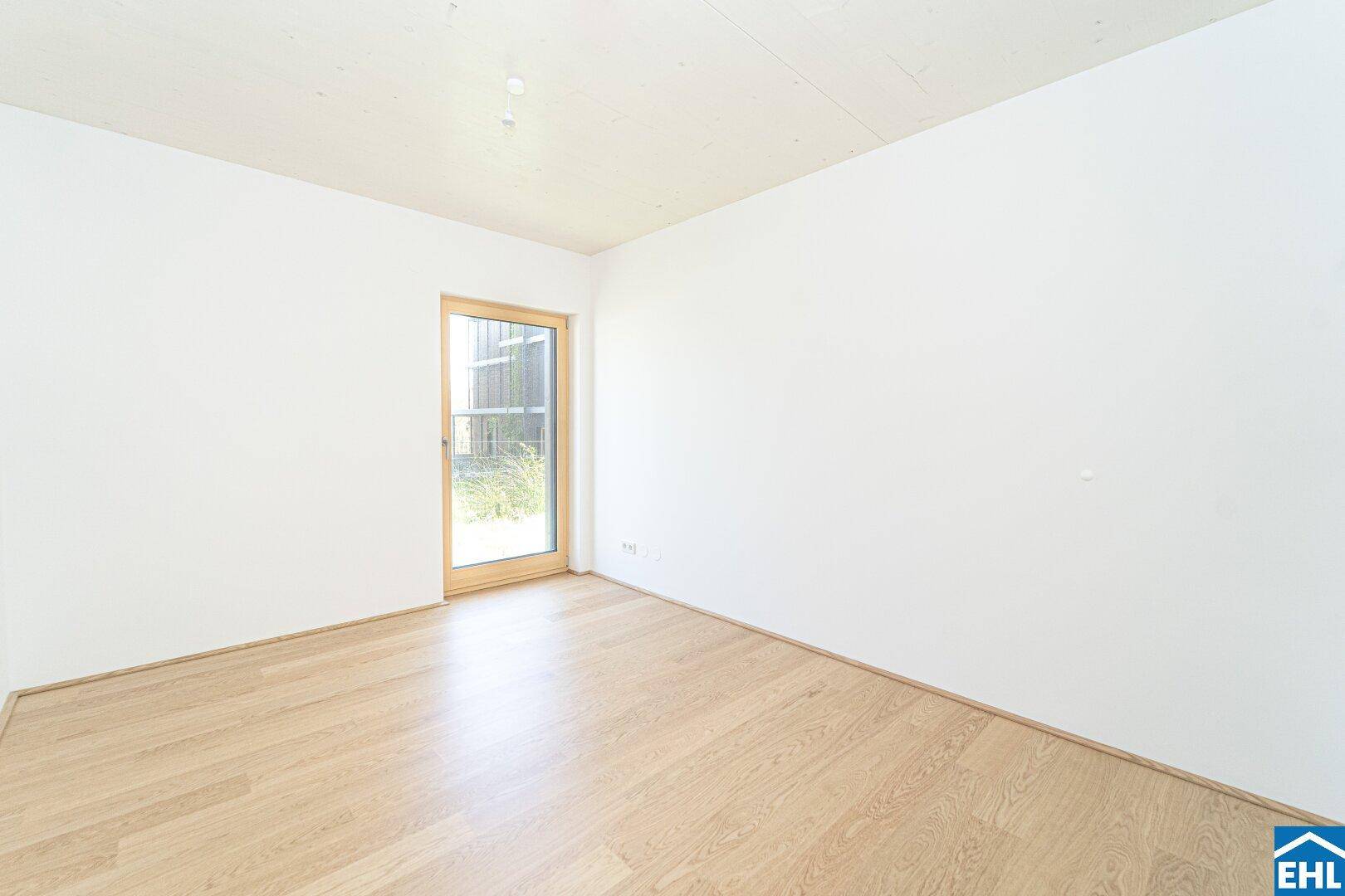 Helles Schlafzimmer mit Parkettboden und Zugang zu einem Außenbereich.