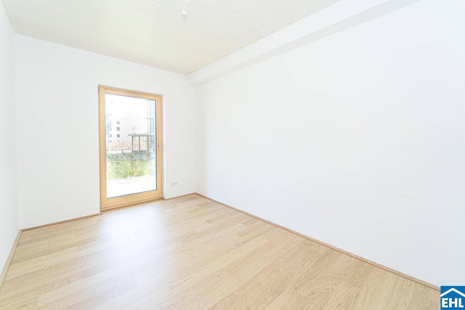Weiteres helles Zimmer mit Parkettboden und einer Tür, die ins Freie führt.