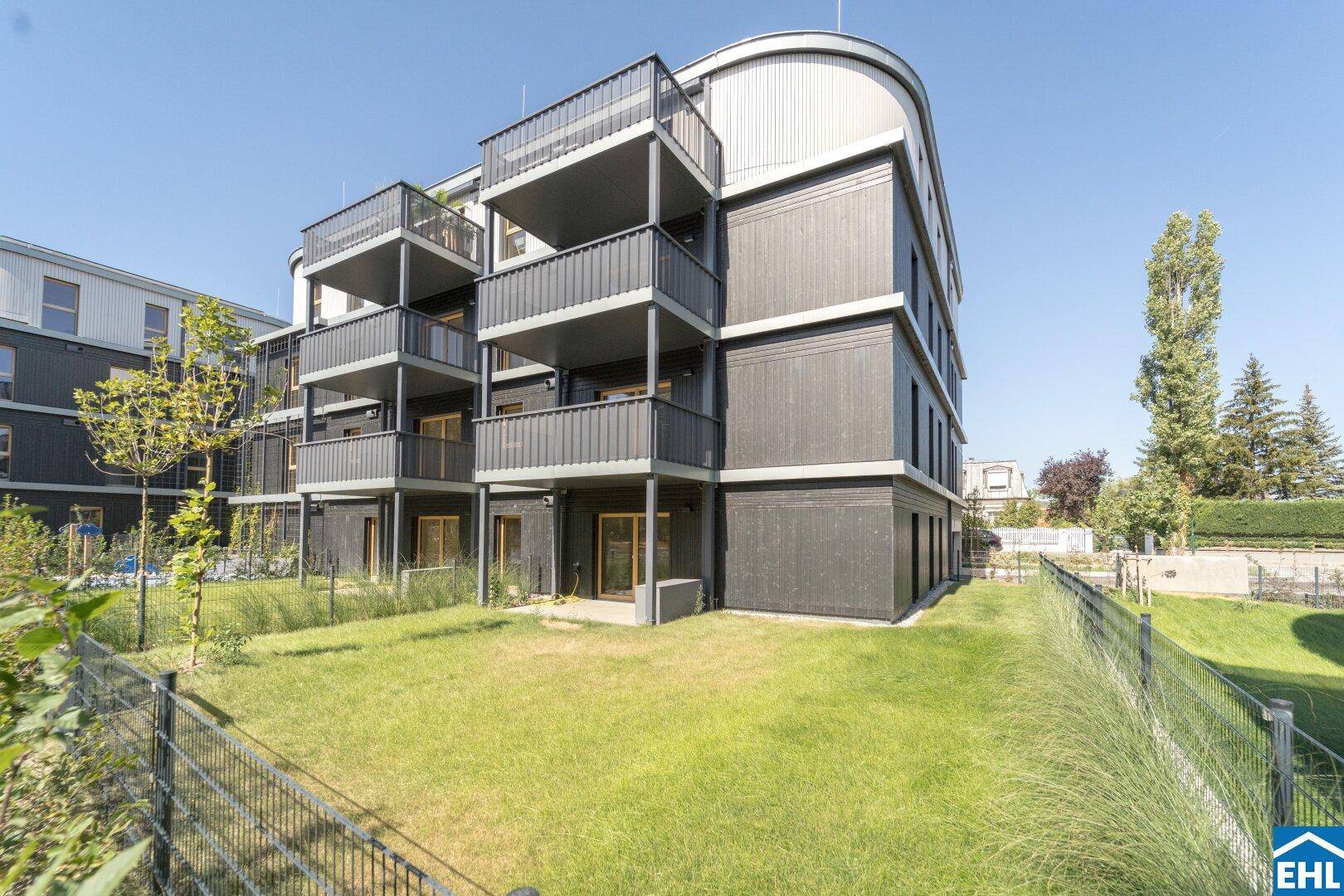 Moderne Wohnanlage mit dunkler Fassade, Balkonen und gepflegten Grünflächen.