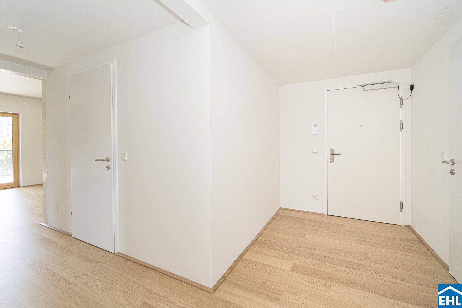 Heller Eingangsbereich mit Holzboden und weißen Wänden, der zu weiteren Räumen führt.