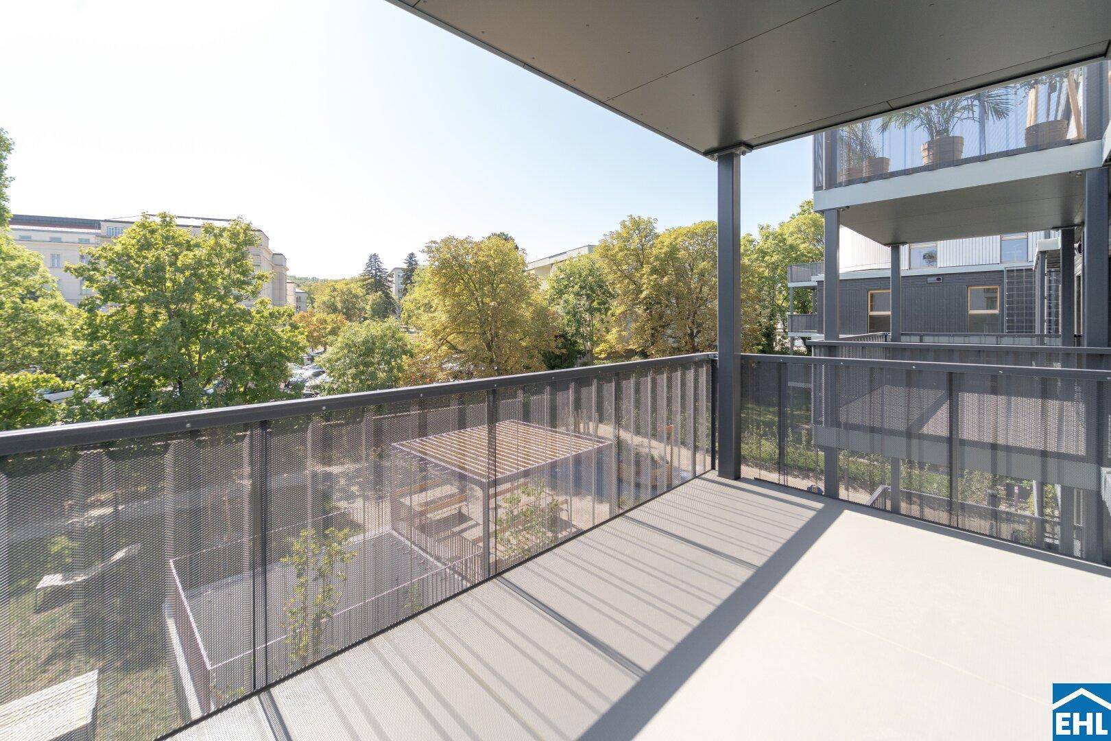 Geräumiger Balkon mit Metallgeländer und Blick auf grüne Bäume und den Innenhof.