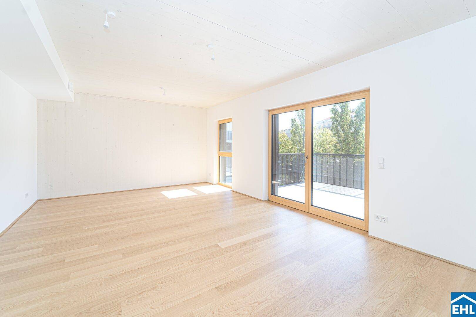Geräumiges, helles Wohnzimmer mit Holzboden und großem Fenster, das viel Tageslicht hereinlässt.