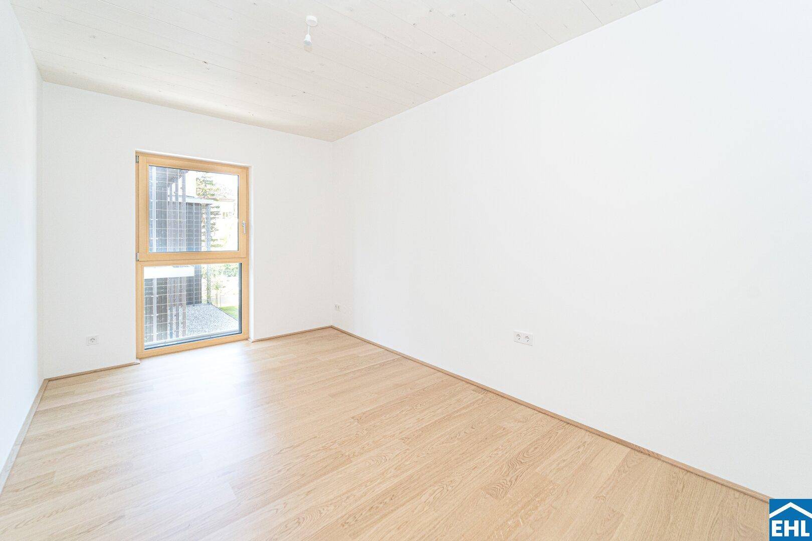 Ruhiges Schlafzimmer mit hellem Holzboden und großem Fenster, das eine angenehme Atmosphäre schafft.