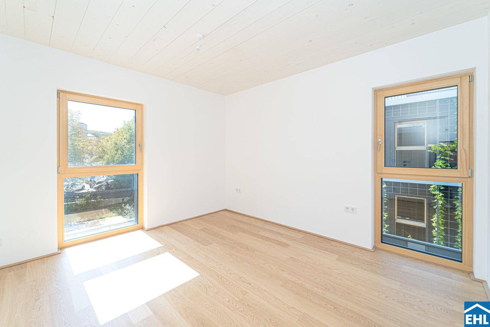 Lichtdurchflutetes Schlafzimmer mit zwei großen Fenstern und hellem Holzboden, ideal für erholsame Nächte.