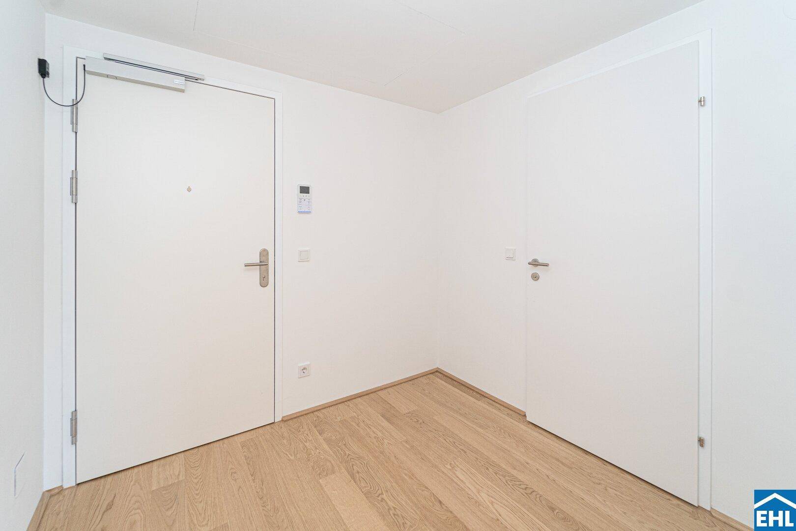 Heller Eingangsbereich mit Holzboden und zwei weißen Türen, die zu den weiteren Räumen führen.